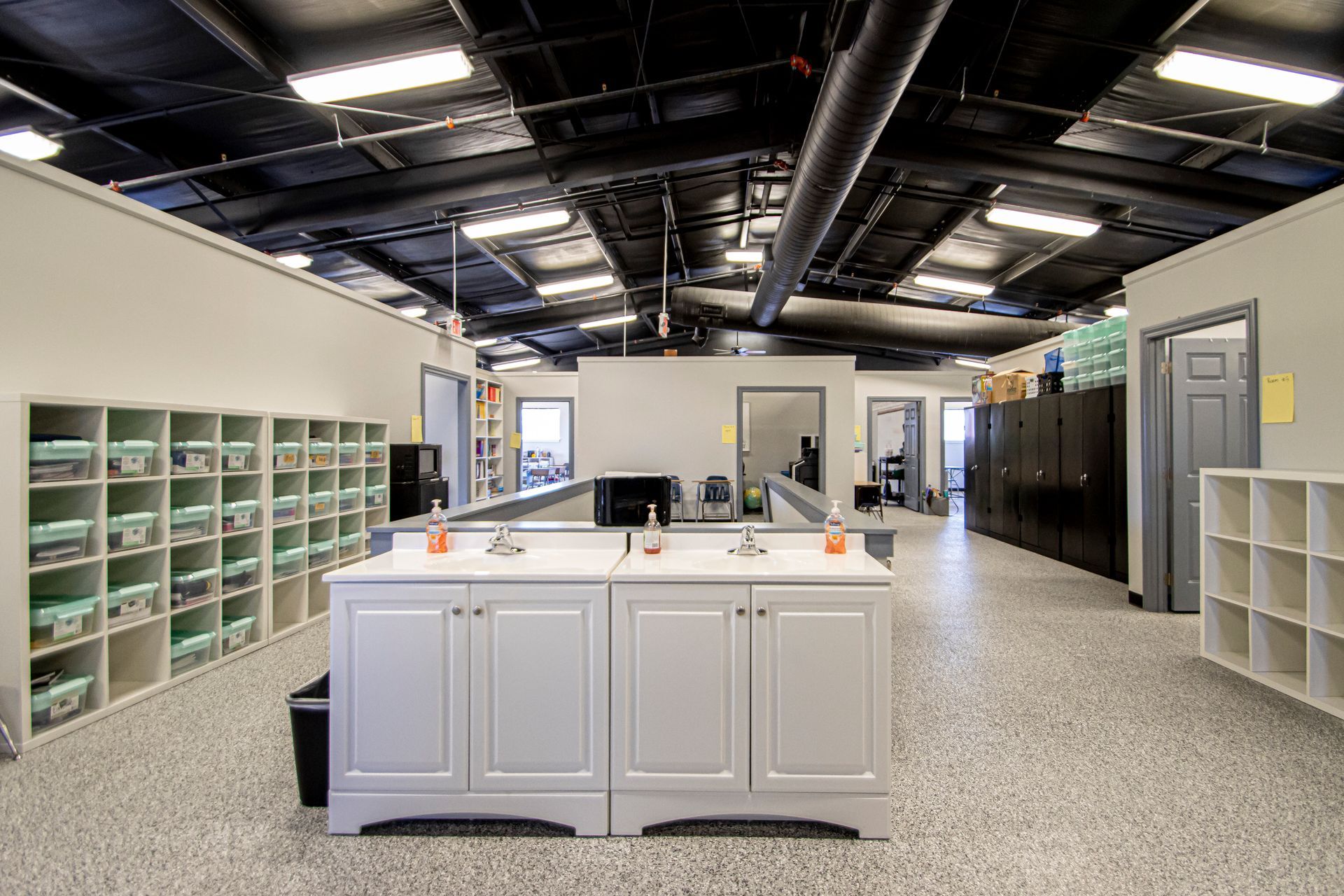 A modern industrial space featuring a double-sink vanity, open white shelving units, and black ceilings with overhead lights.