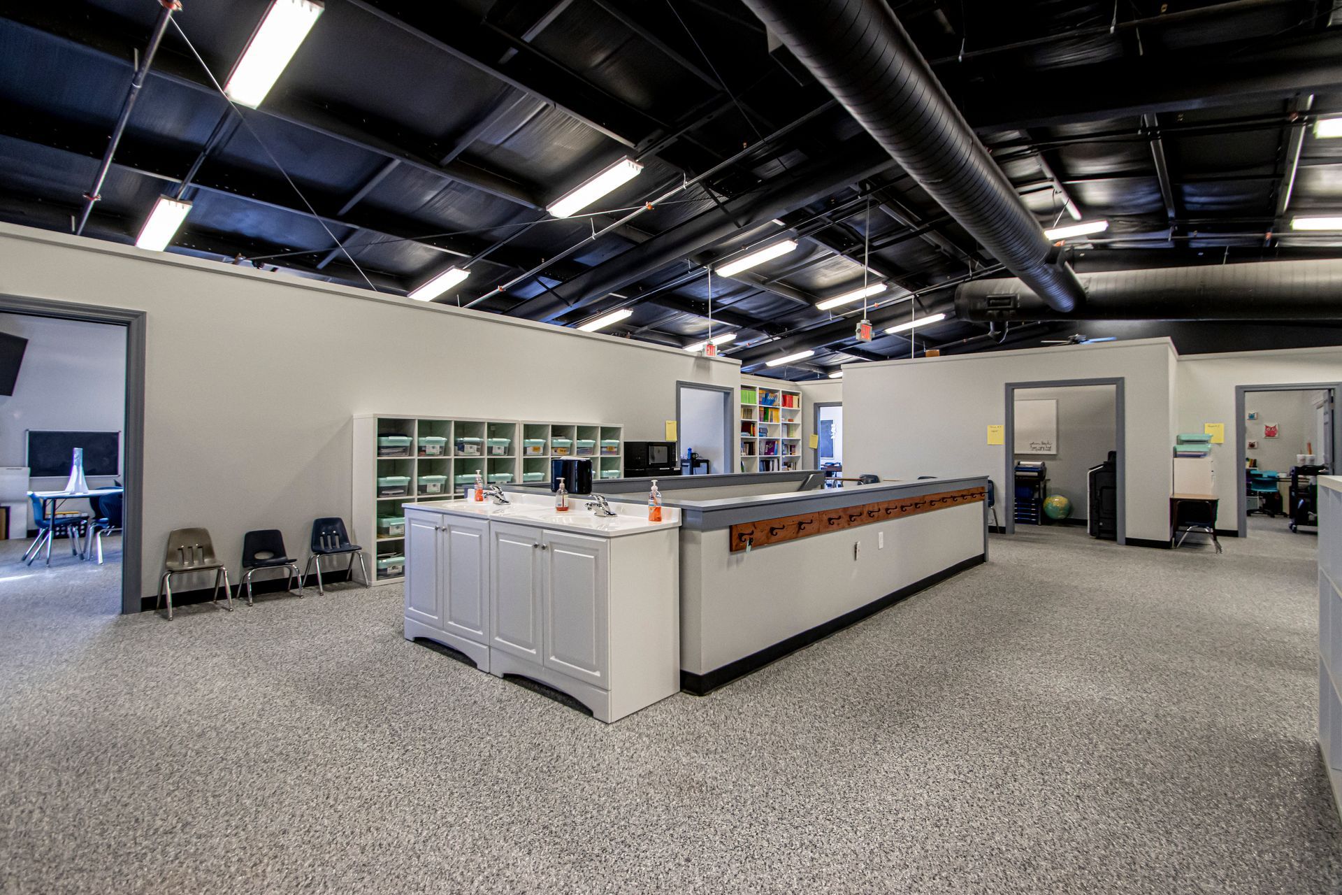 A modern office interior featuring a central white reception desk, grey speckled flooring, and an open, high-ceiling space.