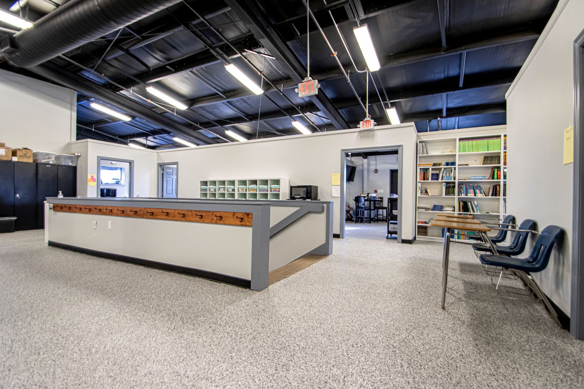 An industrial-style office space with a large central desk, high ceilings with track lighting, and a shelving unit.