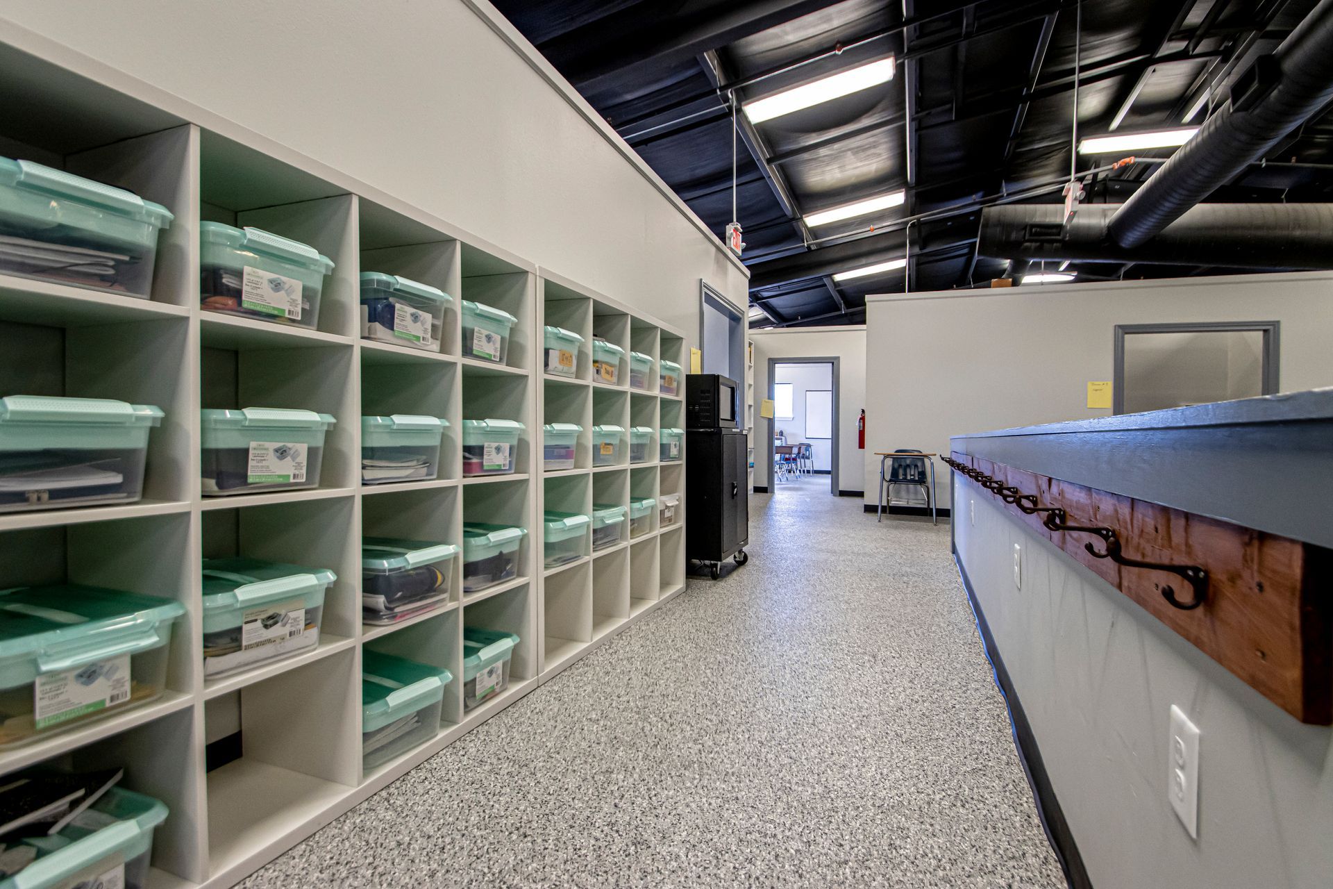 A hallway with a large wall of open storage cubbies holding mint-green bins, and a service counter on the right.