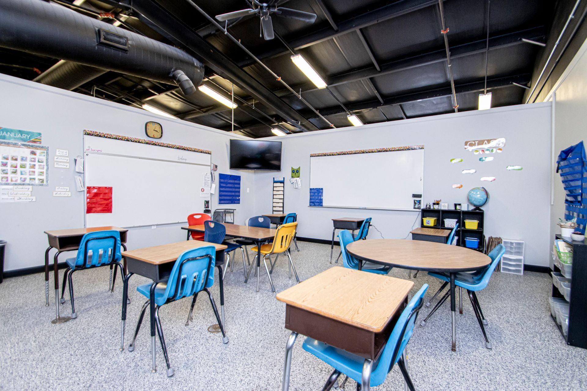 A classroom with student desks, chairs, and two whiteboards on the walls under an industrial-style ceiling.