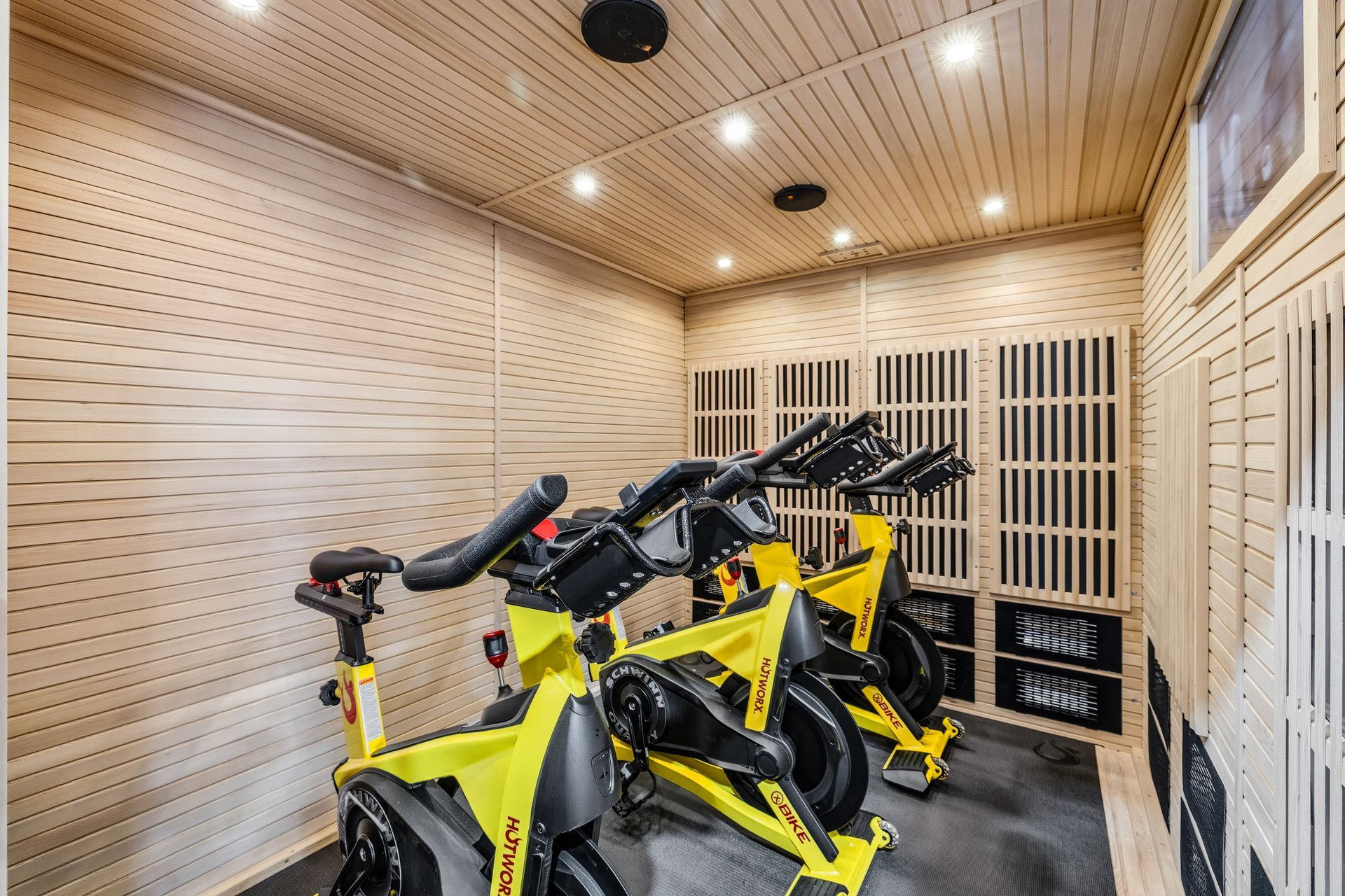 Two bright yellow stationary exercise bikes inside a small room with wood-paneled walls and ceiling.