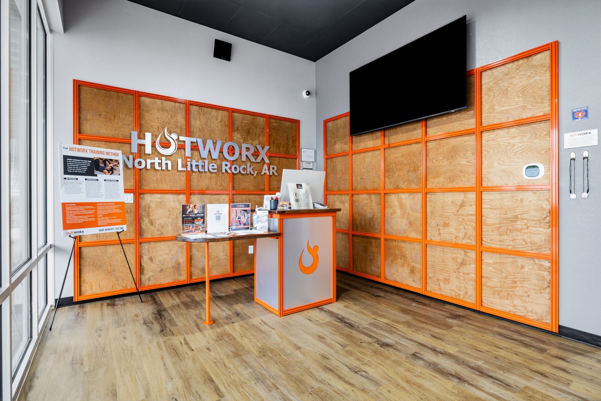 Reception area of a Hotworx studio with orange-framed wooden walls, a service desk, and a television on a gray wall.