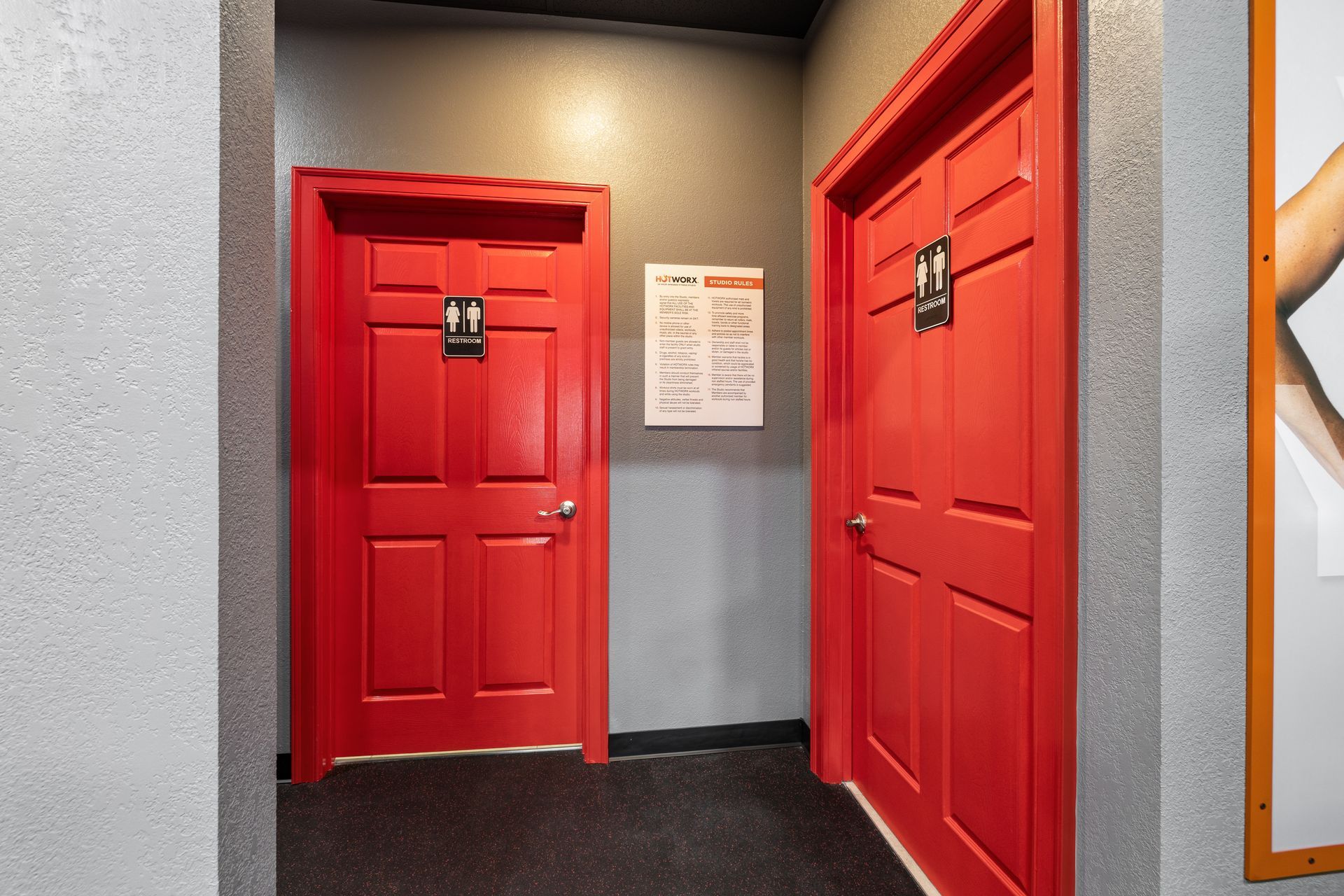 Two vibrant red doors for restrooms side-by-side in a hallway with a sign on the wall between them.