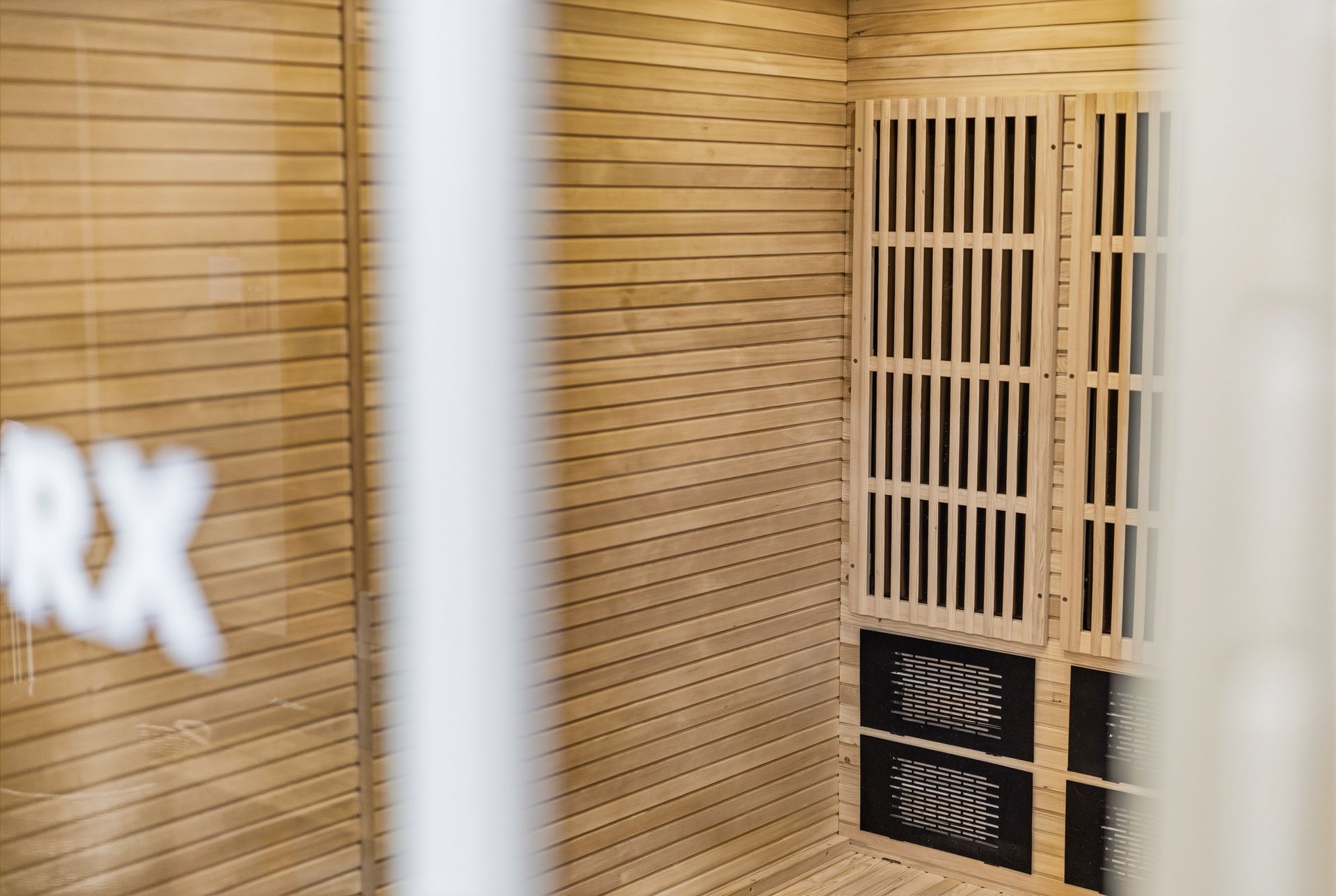 An interior view of a sauna with light-wood slat walls and a heater unit with vertical slats.