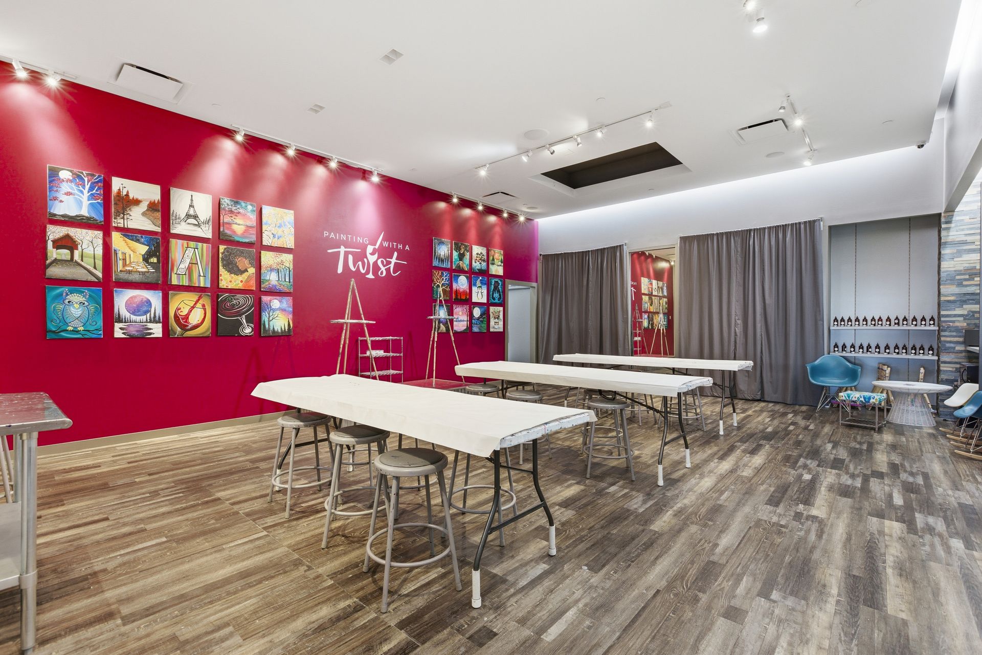 Interior of a painting studio with rows of tables, stools, and walls decorated with square art canvases.