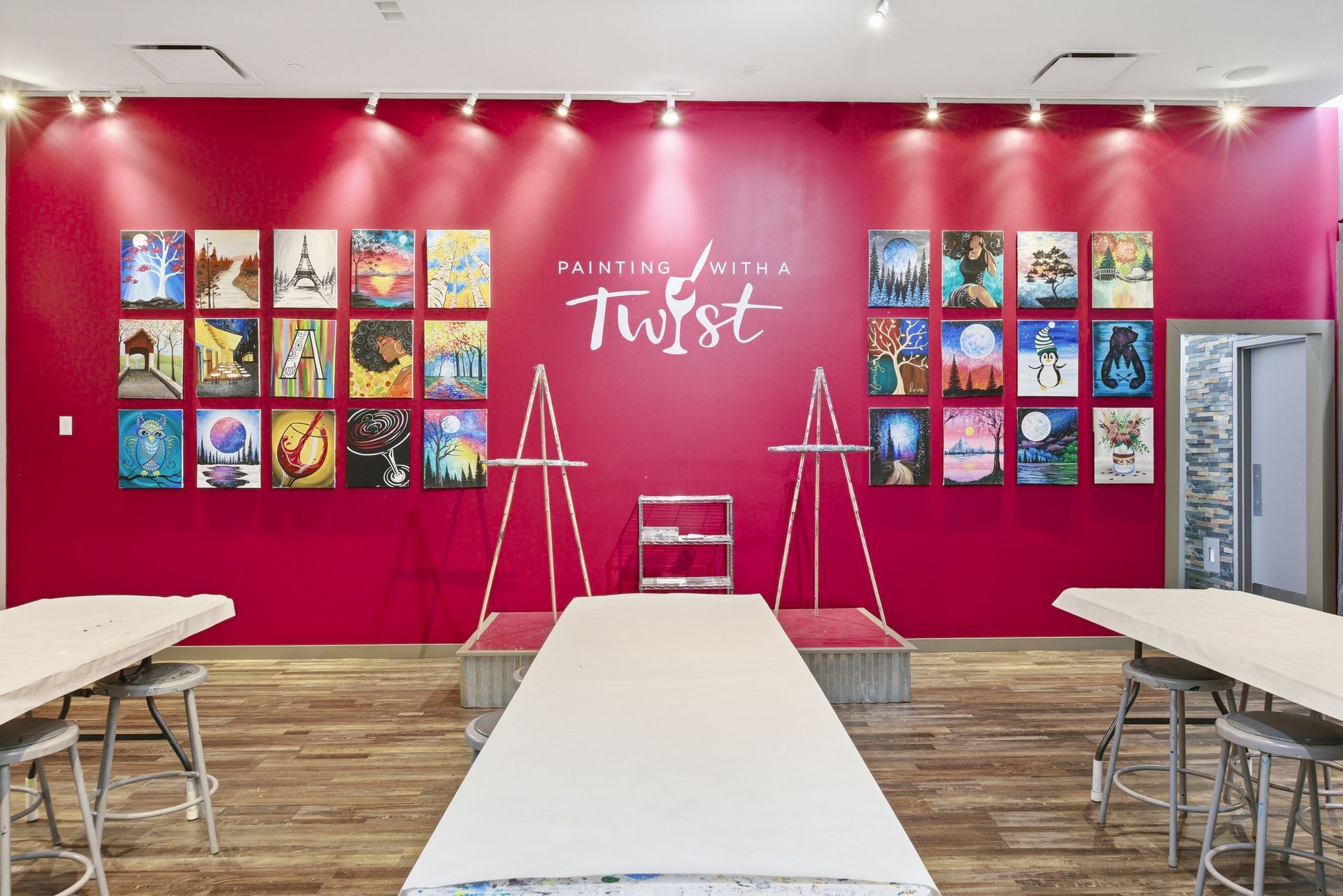 A painting studio with tables and stools, featuring walls lined with colorful canvas art and a central 