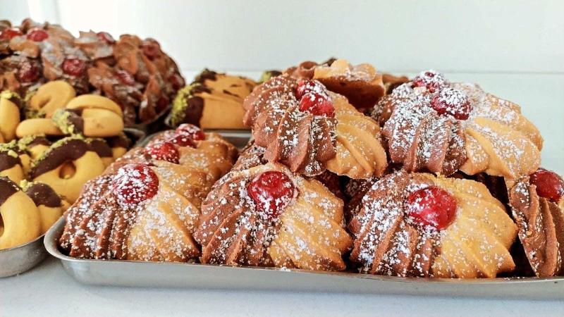 Biscotti su un vassoio, di varie forme, alcuni con cioccolato e ciliegie, spolverati con zucchero a velo.