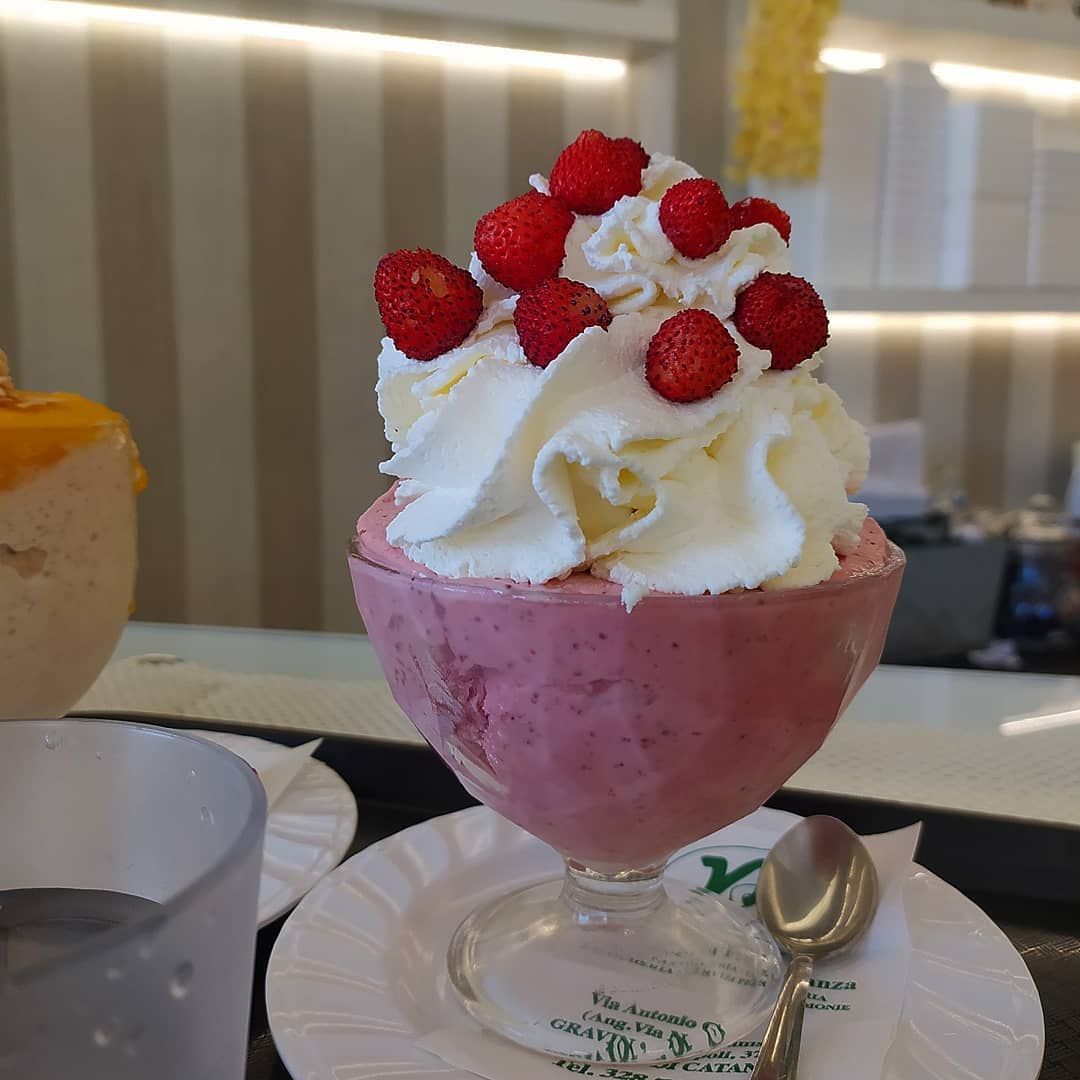 Coppa gelato alla fragola con panna montata e frutti di bosco freschi in un bicchiere.