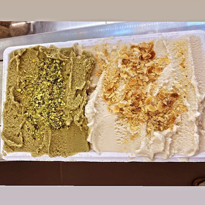 Gelato al pistacchio e alla mandorla in una vaschetta bianca; il gelato al pistacchio è verde con pistacchi tritati, quello alla mandorla è bianco con mandorle tritate.