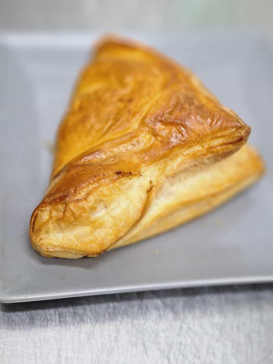 Pasta sfoglia dorata, di forma triangolare, adagiata su un piatto quadrato grigio.