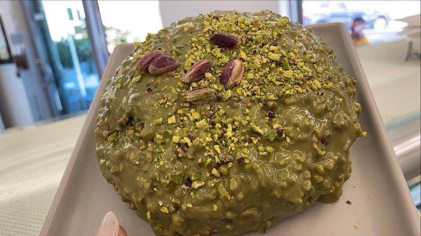 Torta al pistacchio su un piatto rettangolare, guarnita con pistacchi e noci tritati; ambiente interno.