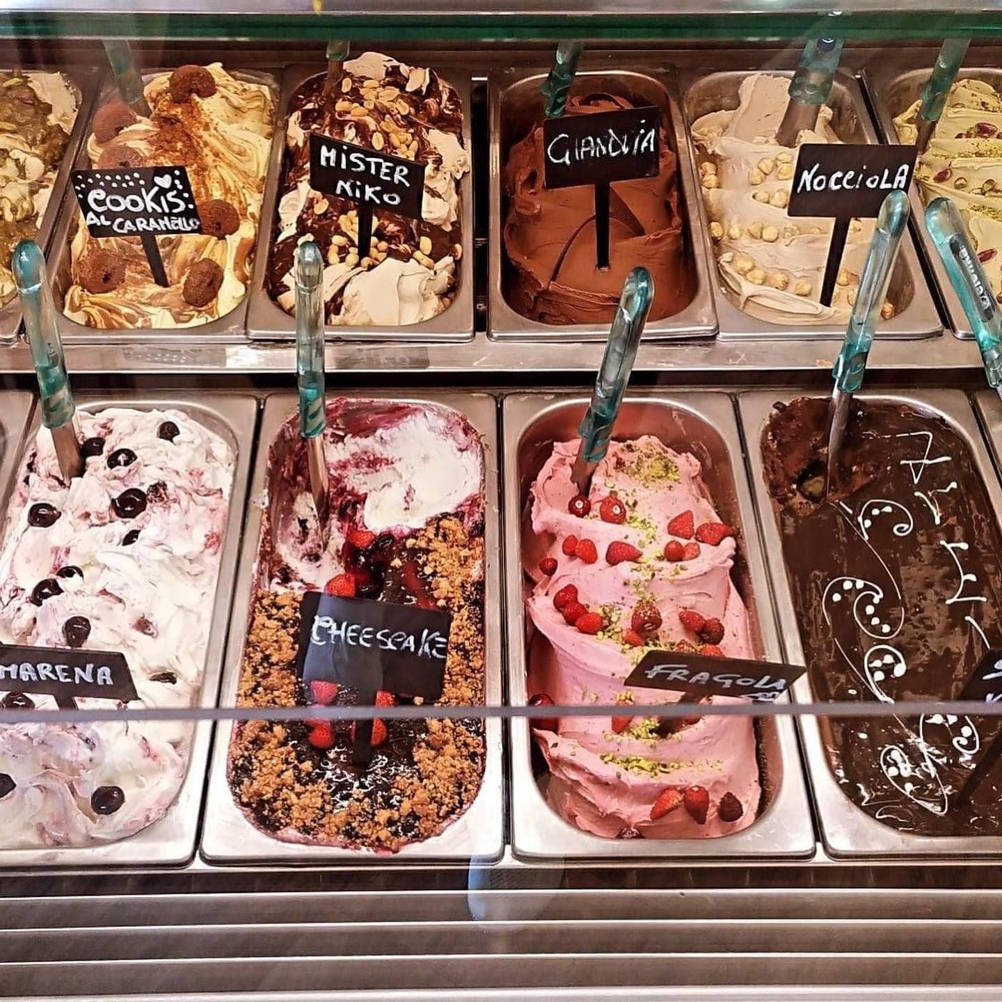 Vetrina per gelati con vari gusti colorati, tra cui cioccolato, fragola e biscotti.
