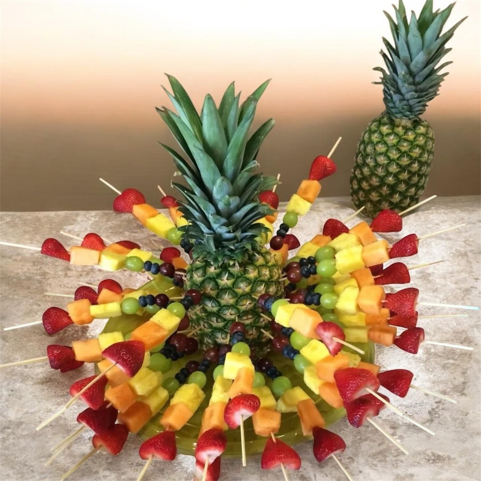 Composizione di ananas con spiedini di frutta su un piatto giallo. Un altro ananas sullo sfondo.