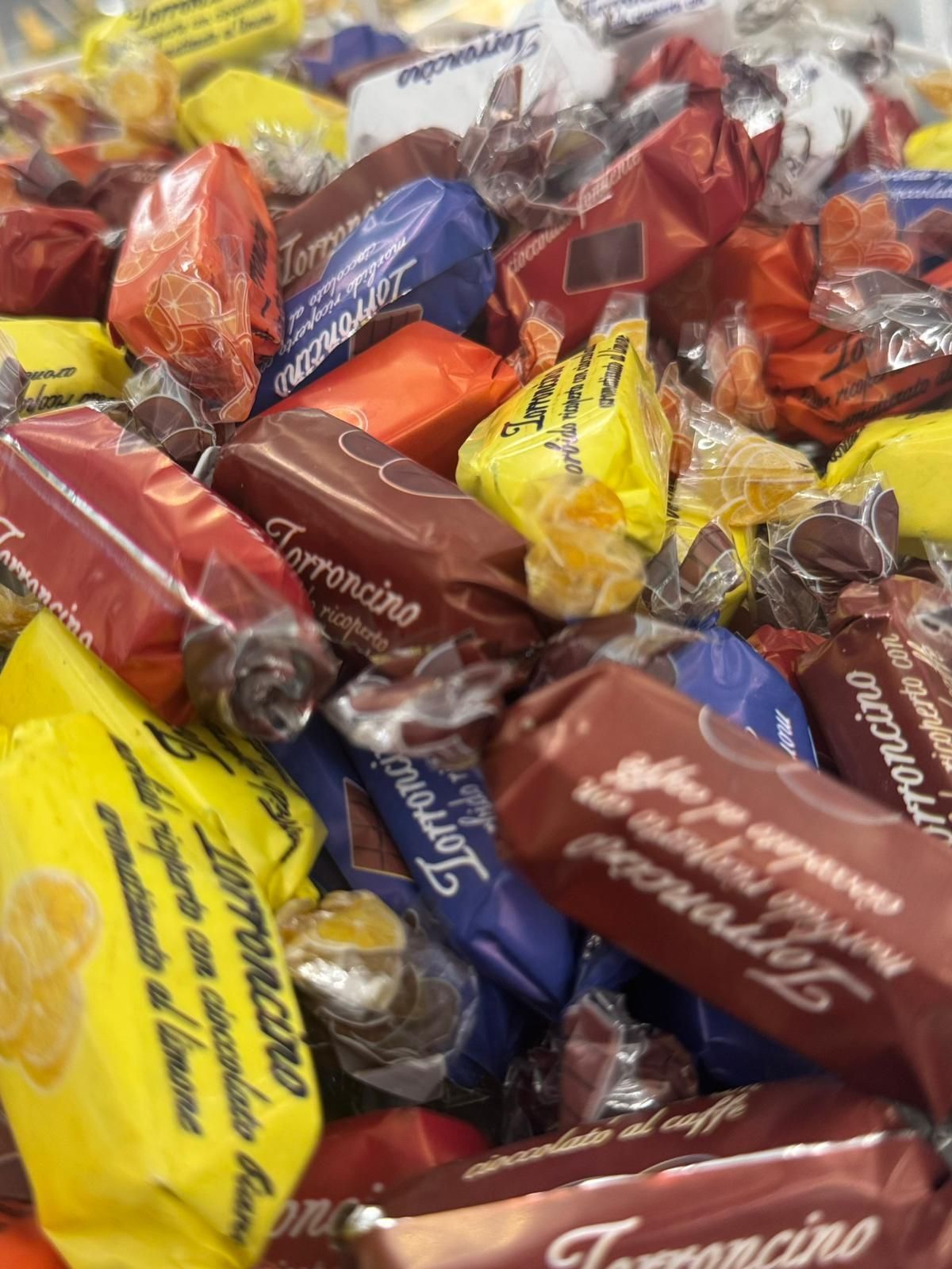 Mucchio di caramelle Torroncino colorate incartate; incarti marroni, gialli, rossi, arancioni e blu.