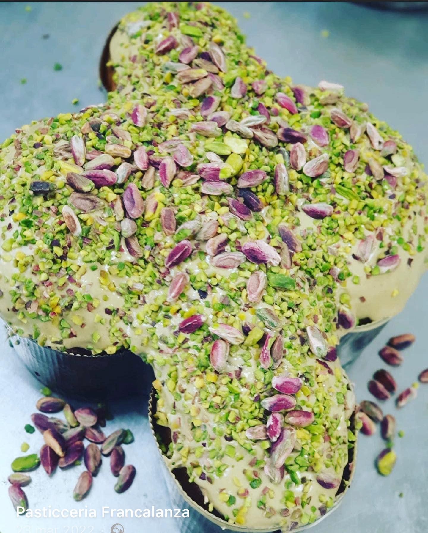 Colomba a forma di croce, ricoperta di crema al pistacchio e pistacchi tritati.