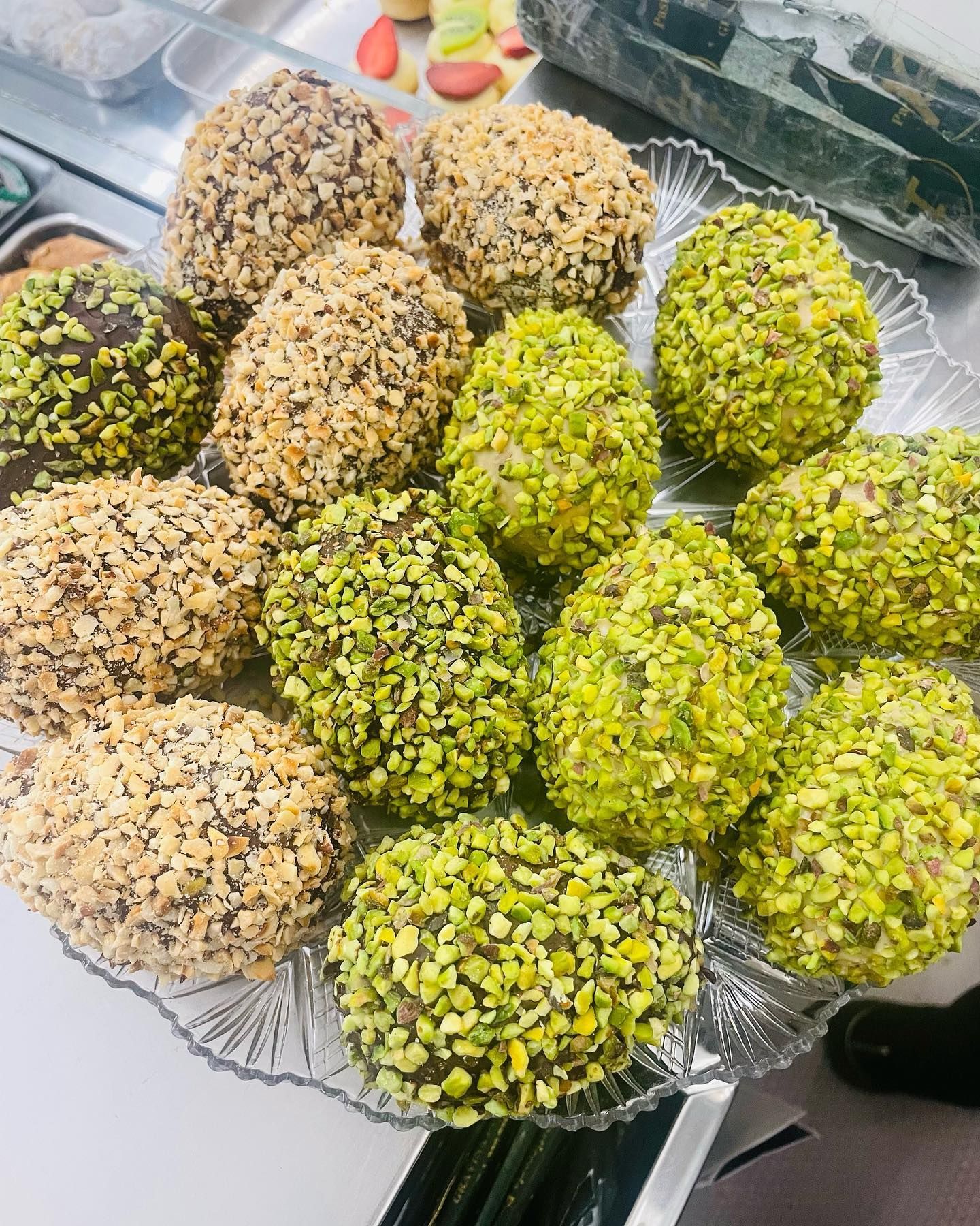 Un piatto di vetro trasparente con un assortimento di dolciumi a forma di palla ricoperti di noci e pistacchi.
