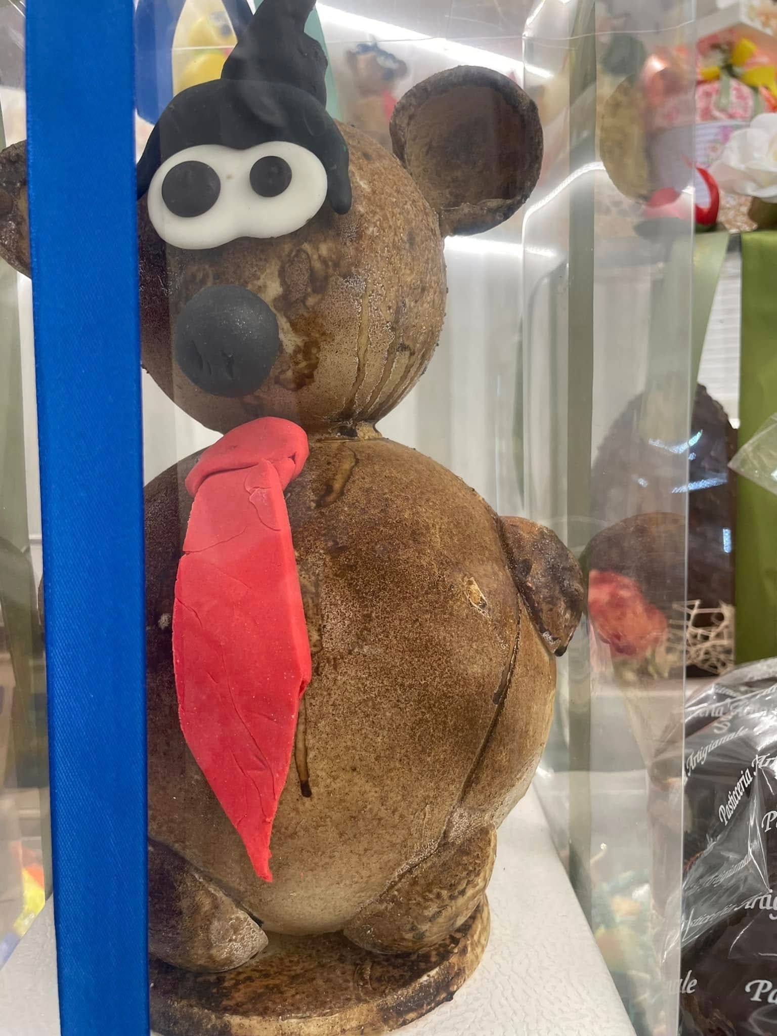 Scultura di un orso di cioccolato con cravatta rossa e cappello nero in una teca.