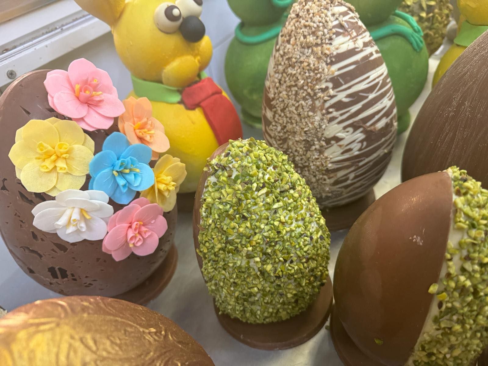 Uova di Pasqua di cioccolato con decorazioni colorate, tra cui fiori e pistacchi.