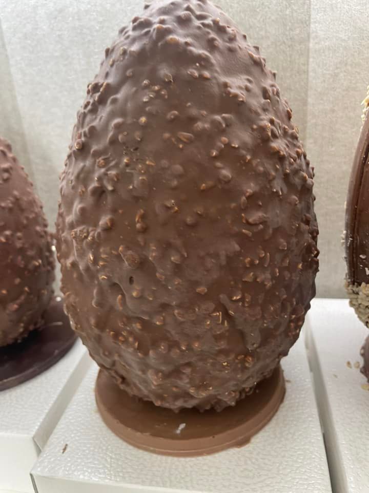 Grande uovo di cioccolato ricoperto da una glassa testurizzata, poggiato su una base circolare.