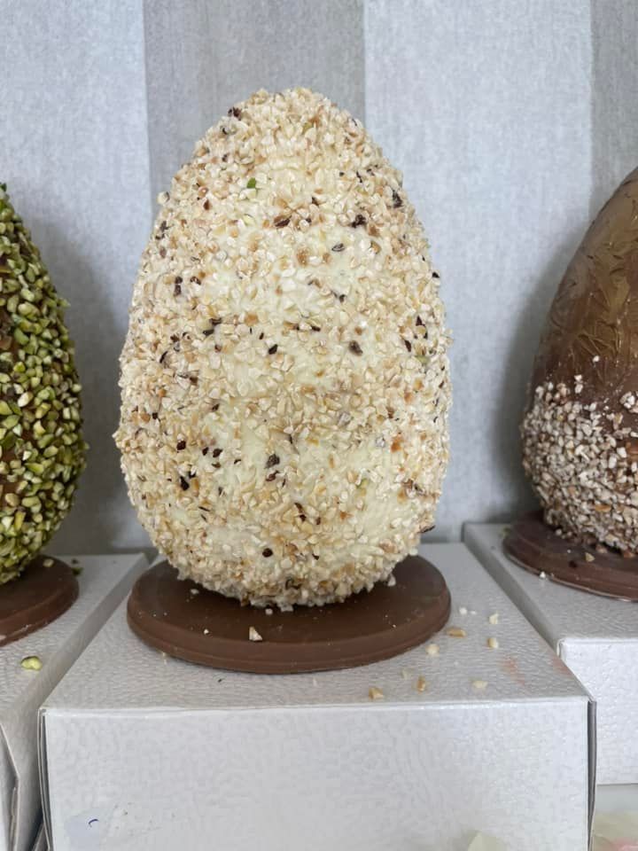 Uovo di cioccolato ricoperto di noci tritate, su una base di cioccolato, esposto insieme ad altre uova di cioccolato decorate.