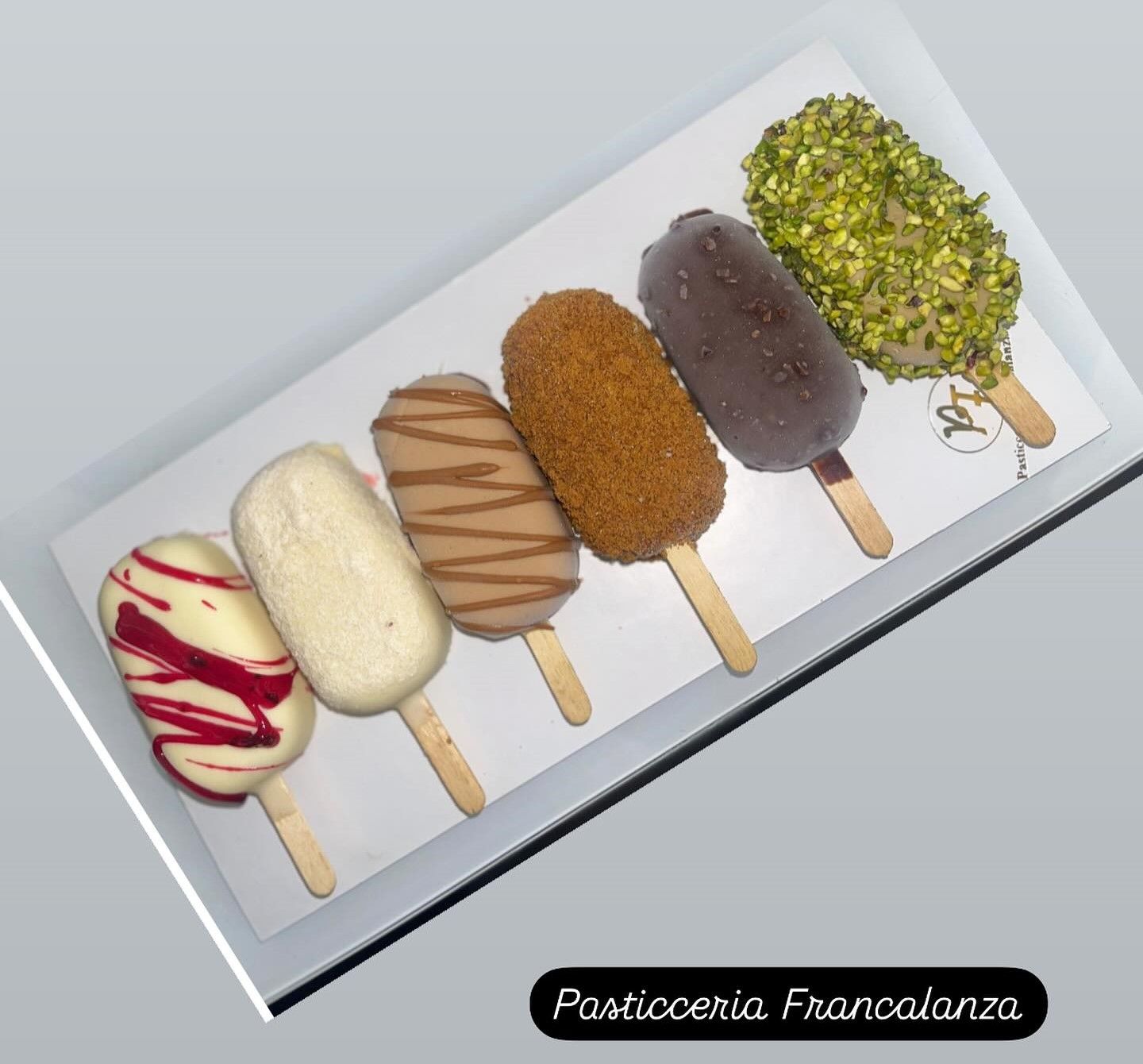 Sei dessert a forma di ghiacciolo con diverse ricoperture su un vassoio.