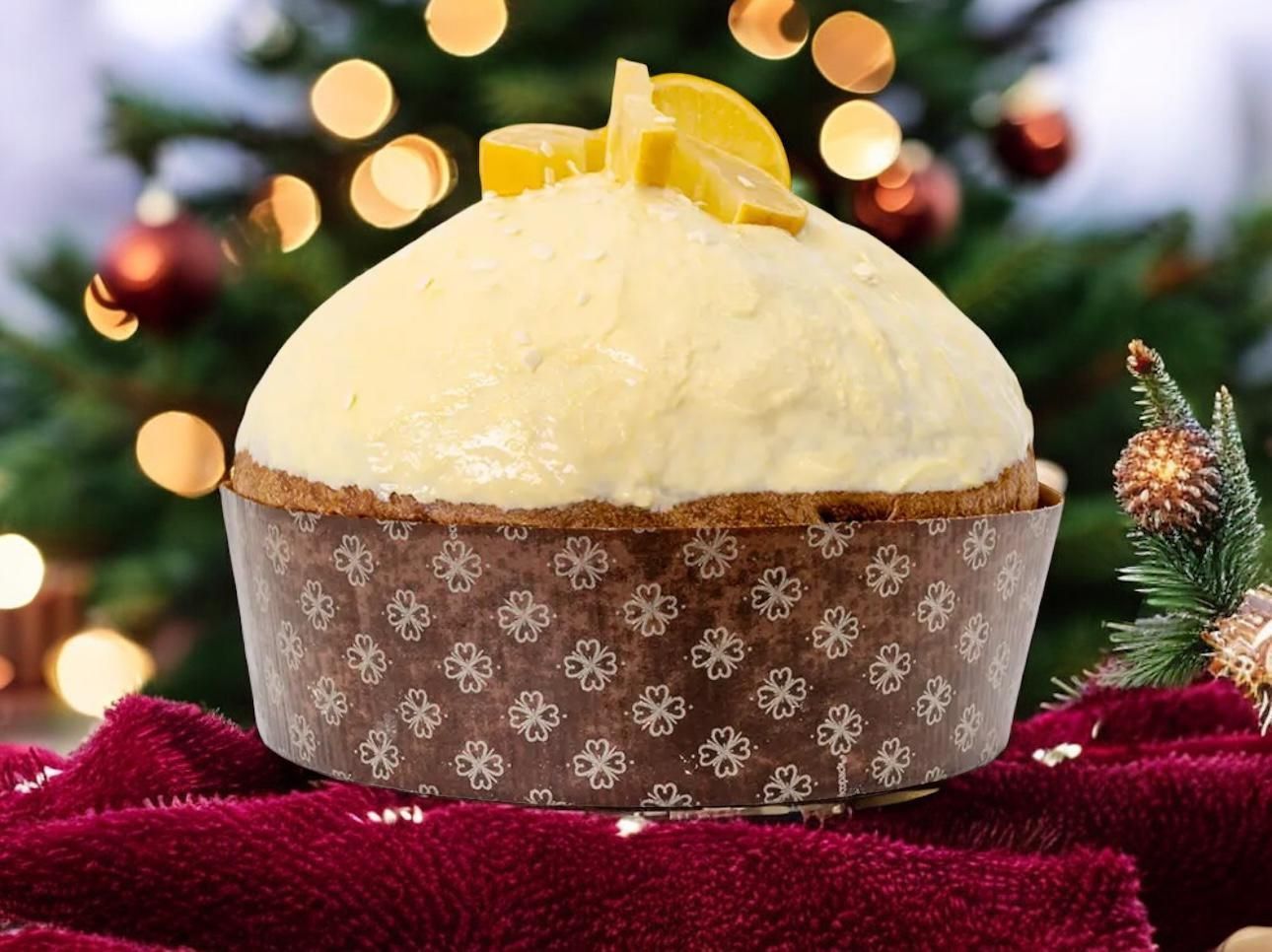Panettone con glassa bianca e fette di limone sopra, davanti a un albero di Natale decorato.