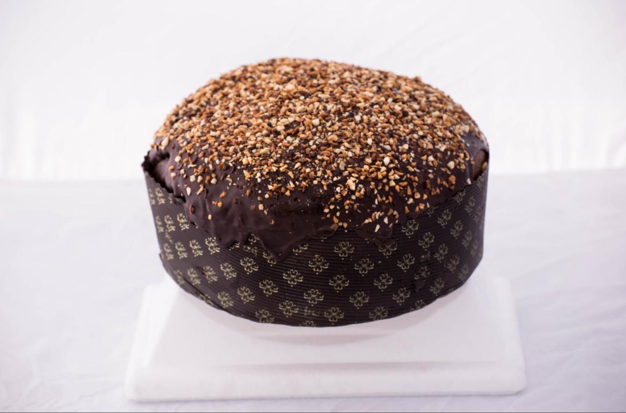 Panettone al cioccolato con guarnizione di noci, avvolto in carta e appoggiato su una superficie bianca.