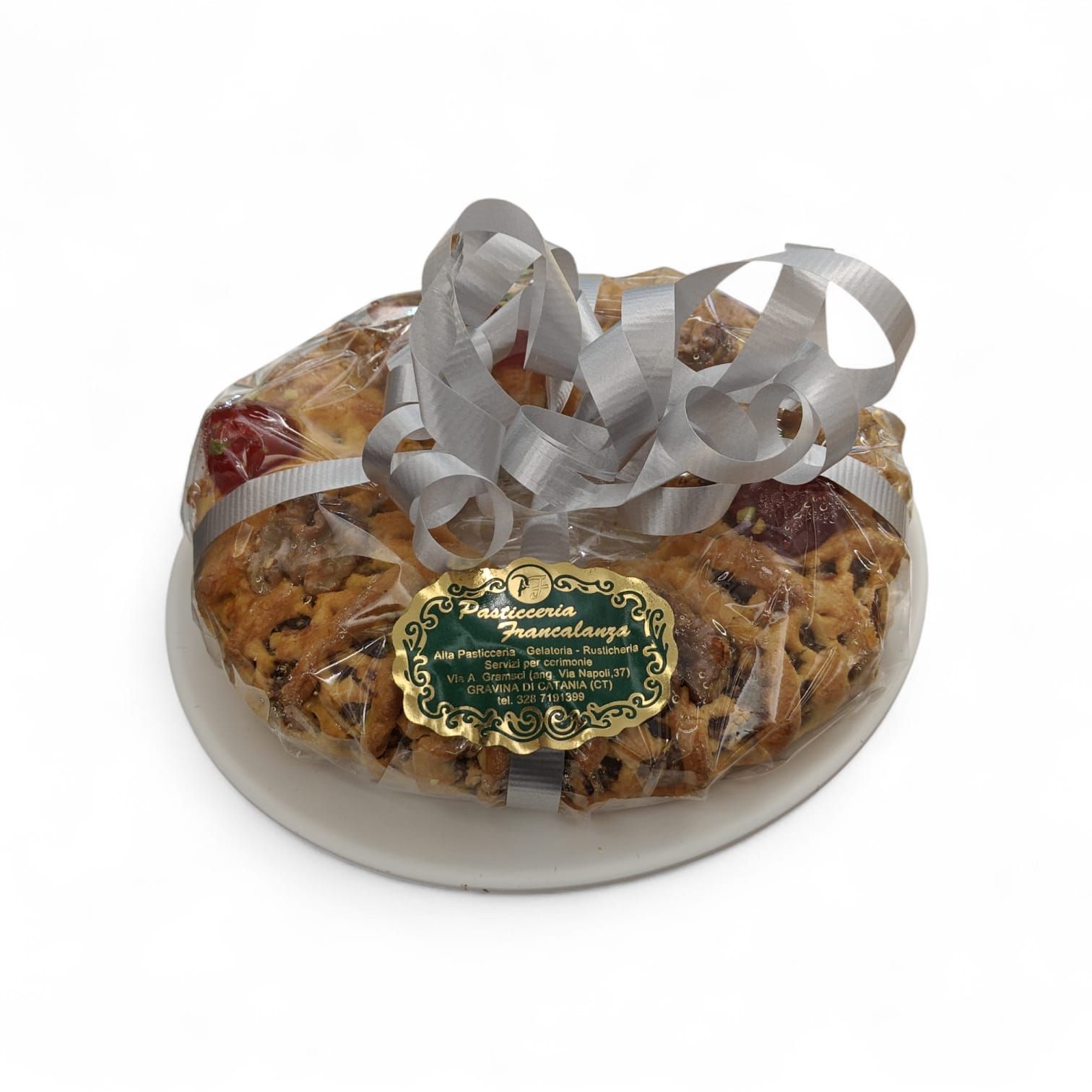 Pan di frutta avvolto in plastica trasparente su un piatto bianco, legato con un nastro argentato e un'etichetta.