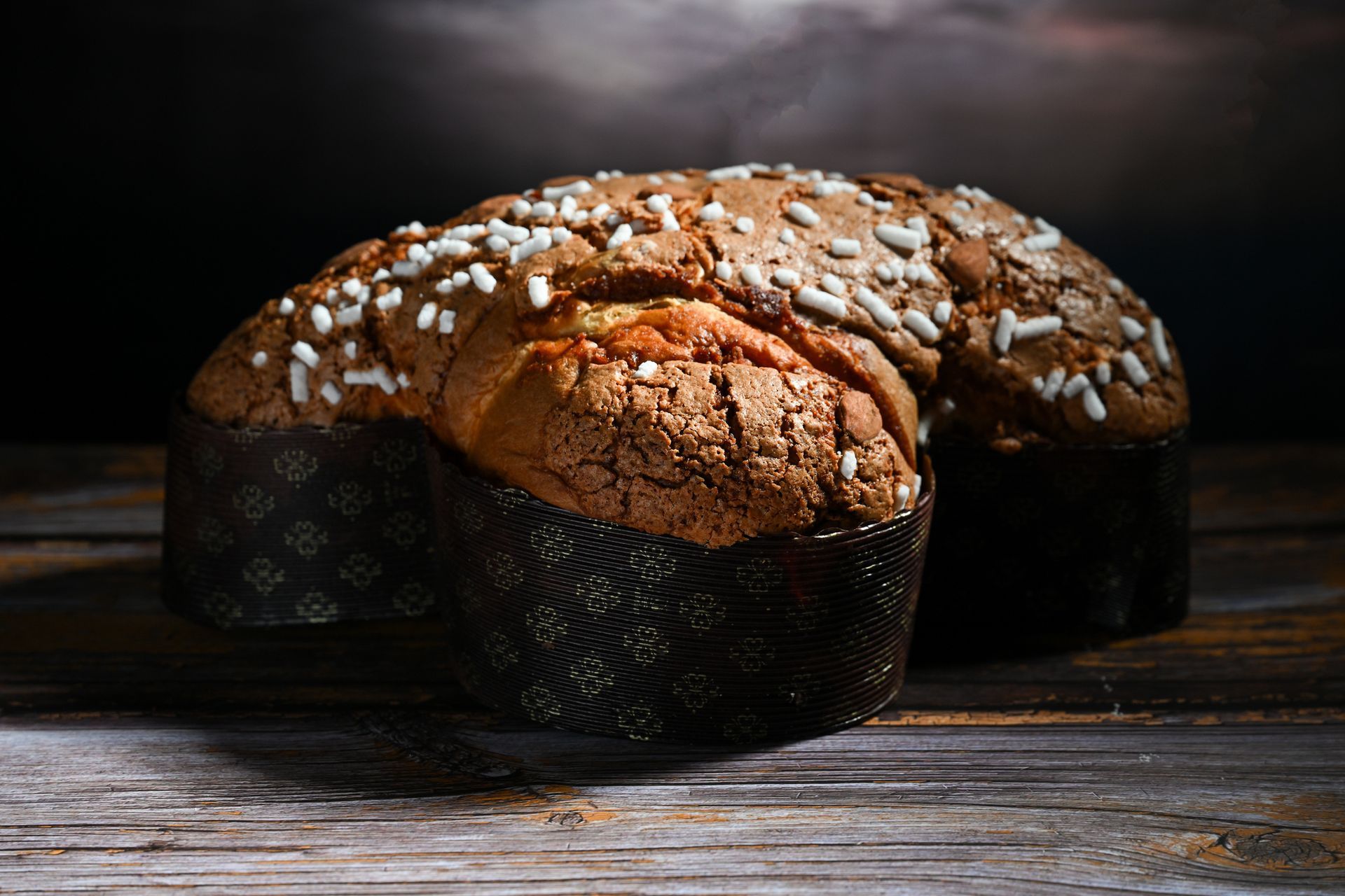 Panettone, un pane dolce, confezionato in carta, cosparso di cristalli di zucchero, su una superficie di legno.