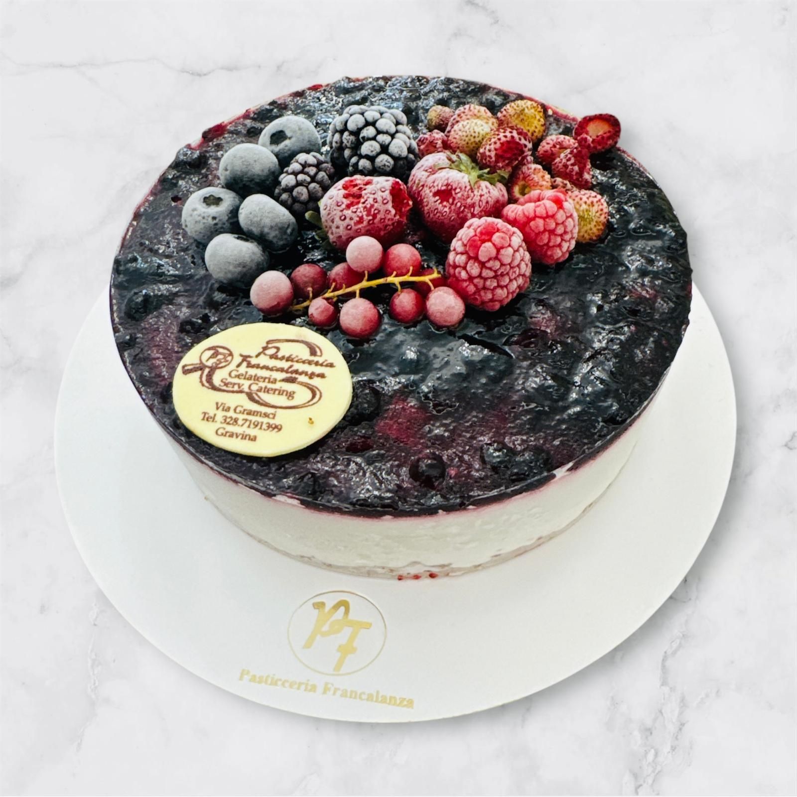 Cheesecake ai frutti di bosco con glassa scura e frutti di bosco glassati, servita su un piatto bianco.