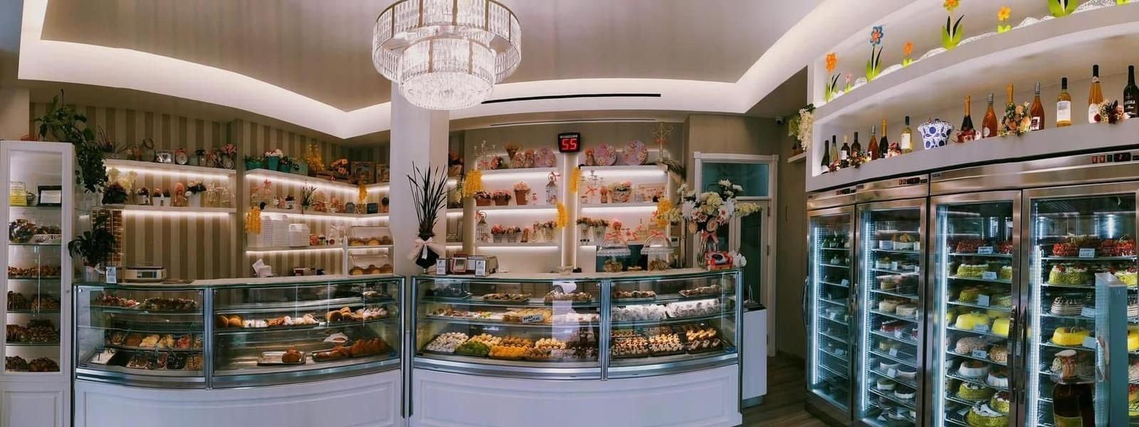 Un interno di panetteria ben illuminato con vetrine di dolci e scaffali pieni di vari articoli.