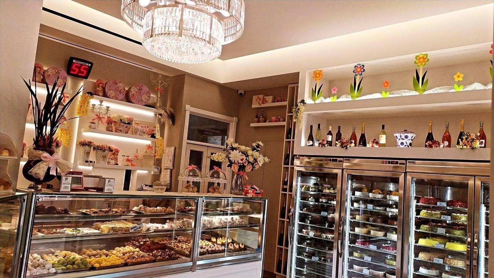 Interno di una pasticceria con vetrine, scaffali con prodotti e un refrigeratore per il vino.