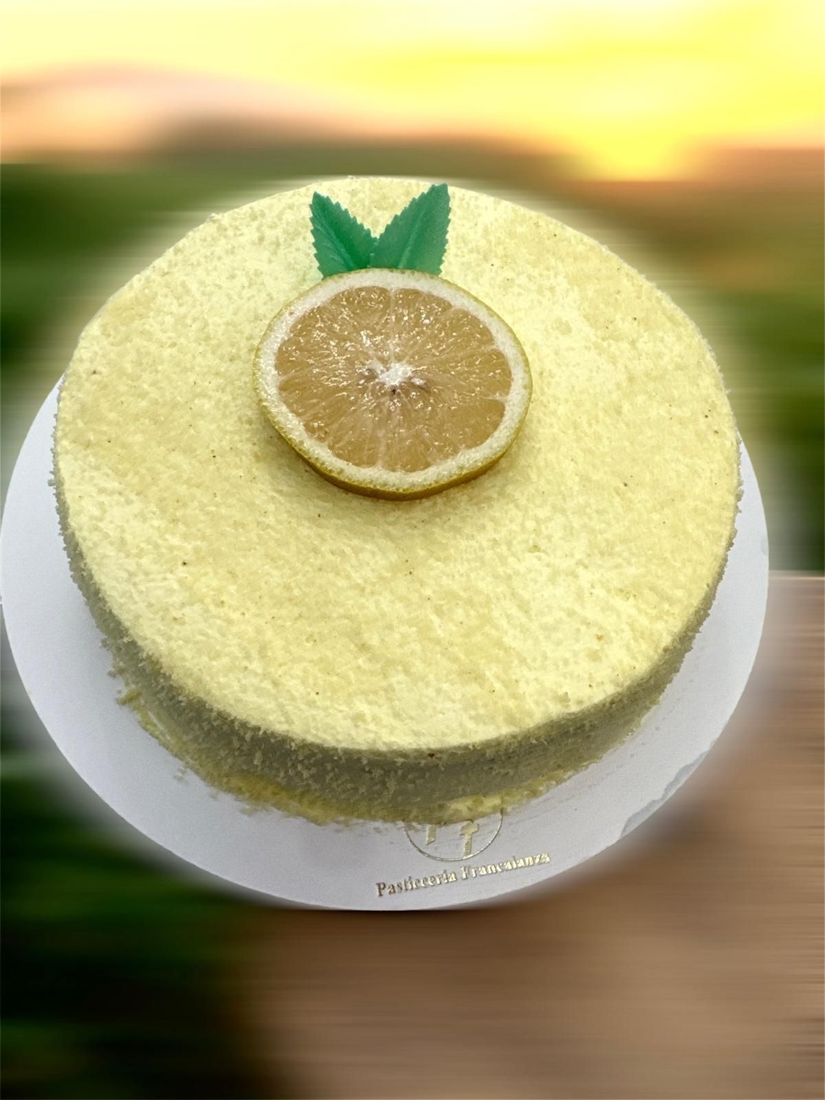 Torta al limone con fette di limone e guarnizione di foglie verdi su un piatto bianco, all'aperto.