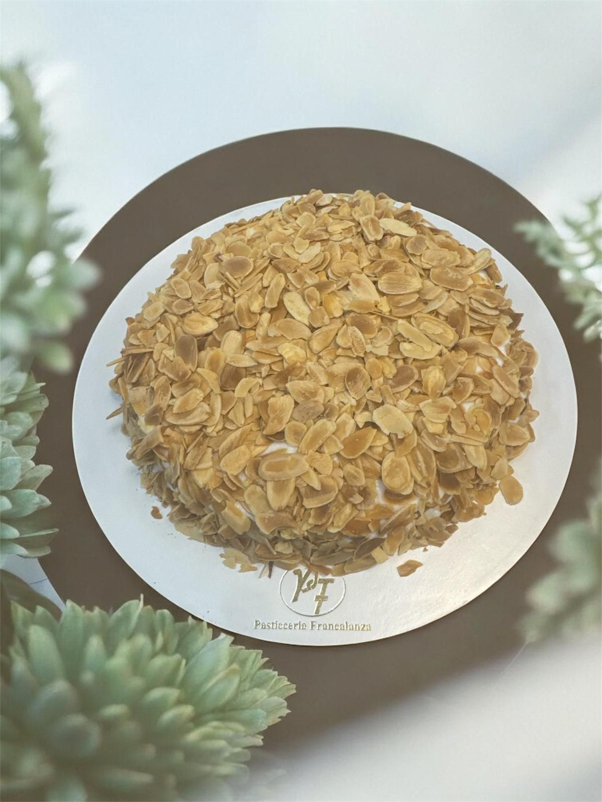 Torta ricoperta di scaglie di mandorle tostate su un vassoio argentato, circondata da piante grasse.