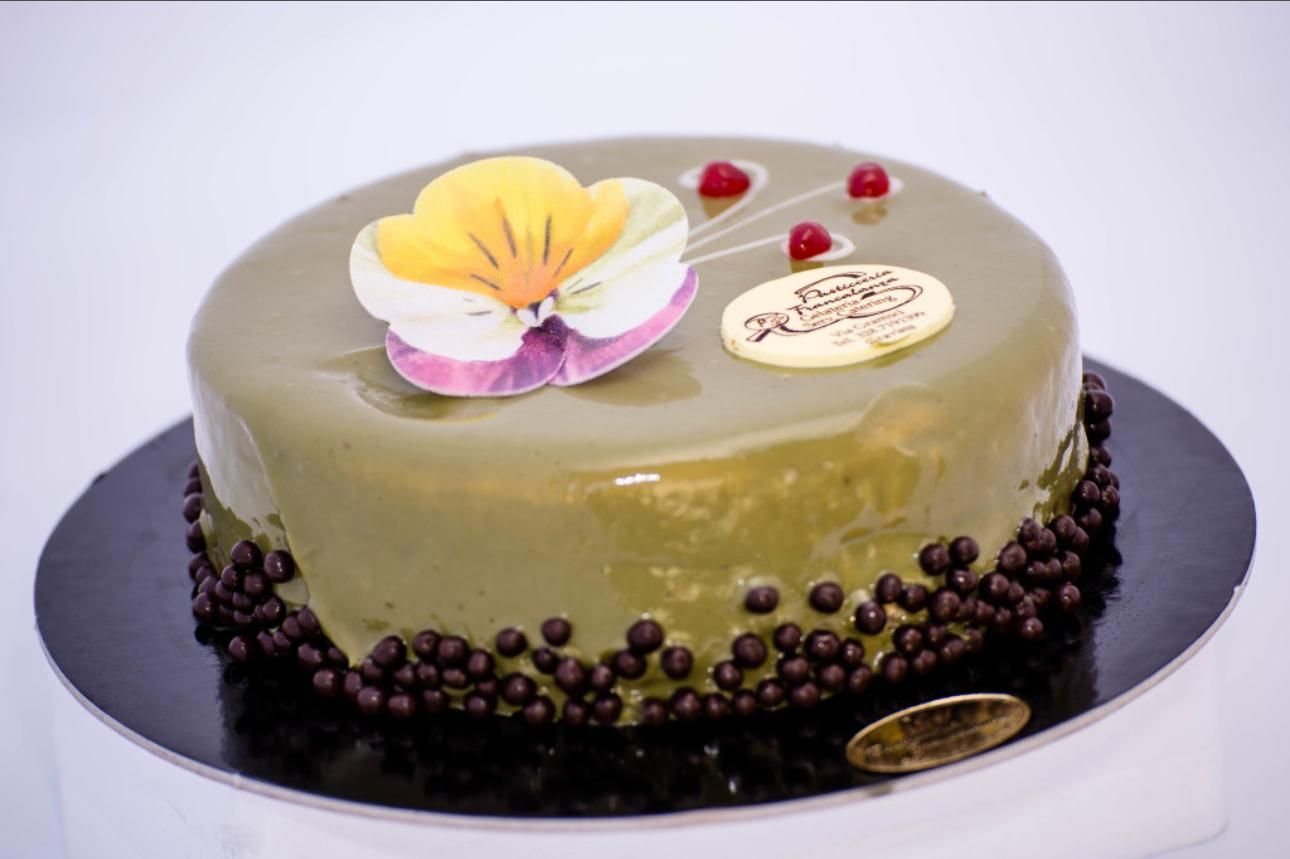 Torta rotonda glassata di verde con palline di cioccolato, guarnita con un fiore e bacche.