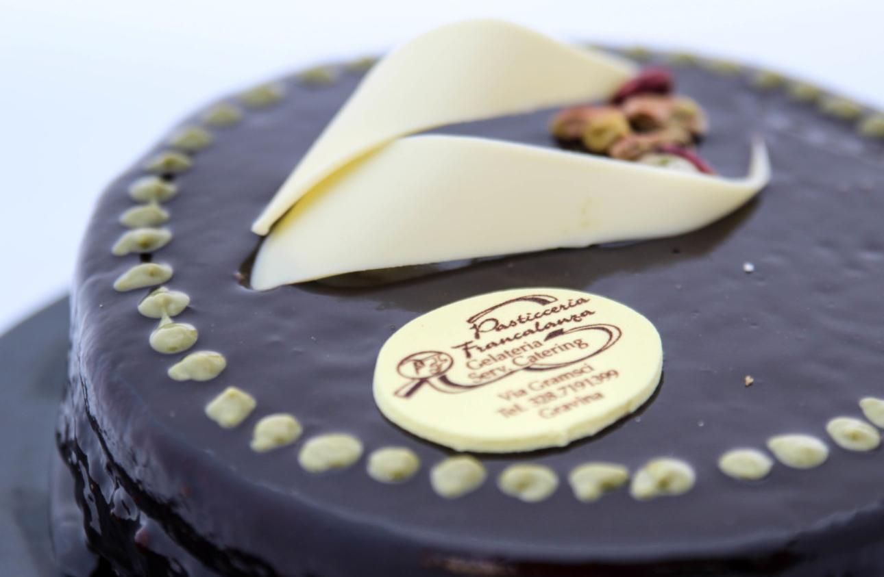 Torta al cioccolato con riccioli di cioccolato bianco e logo sulla parte superiore.