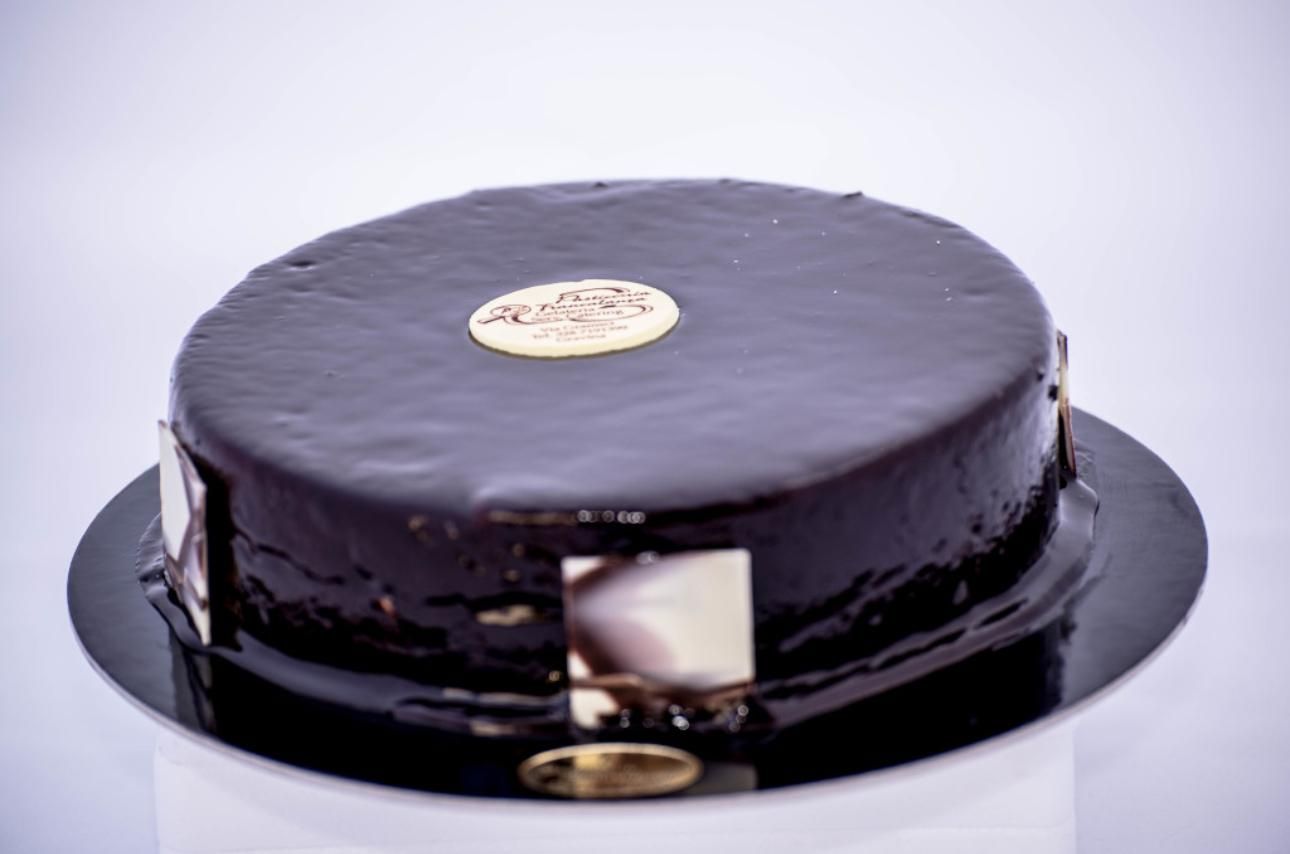 Torta al cioccolato con glassa lucida, su un piatto nero, con dettagli dorati.