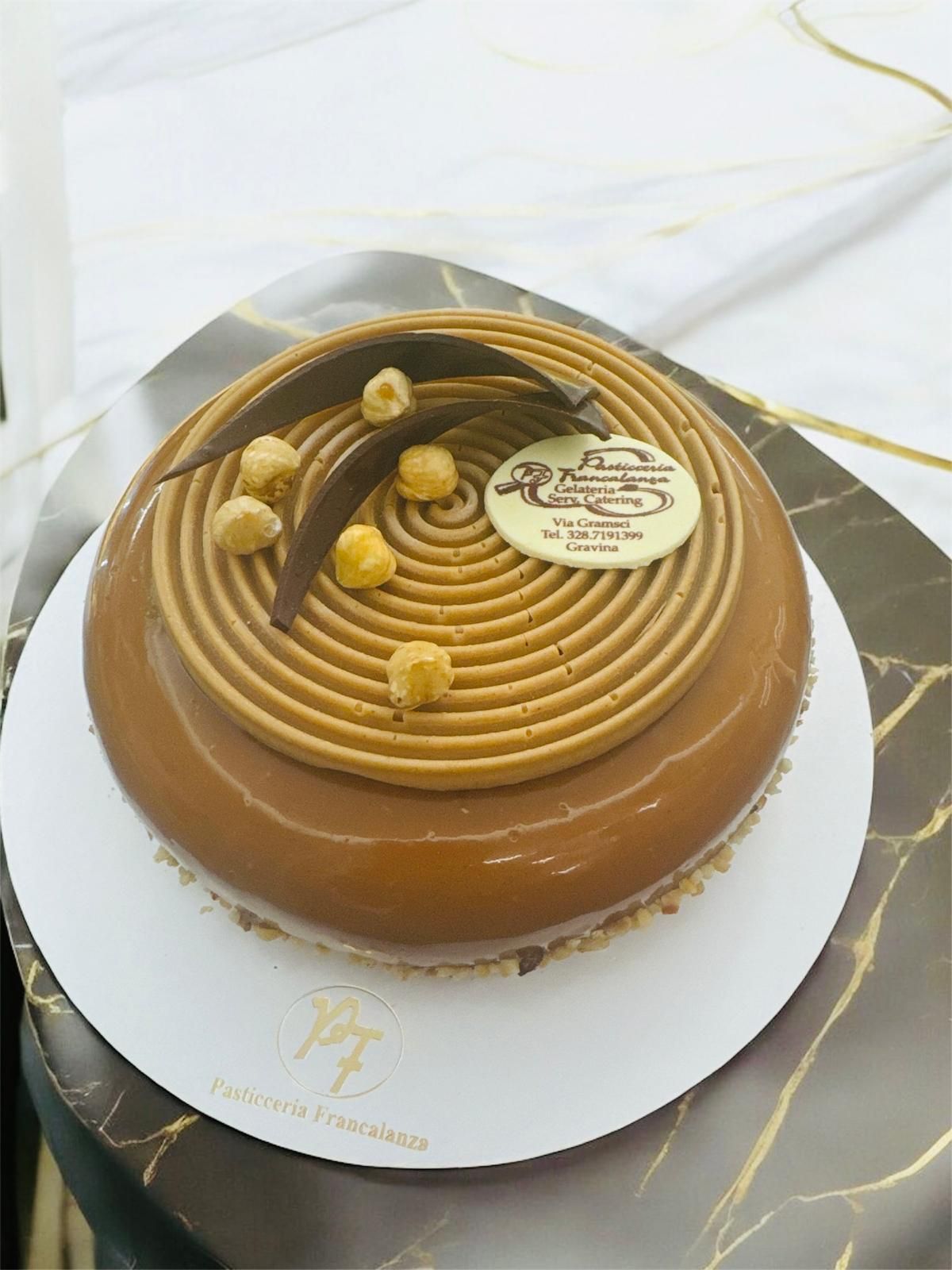 Torta al cioccolato e caramello con decorazioni di nocciole, su piatto bianco.