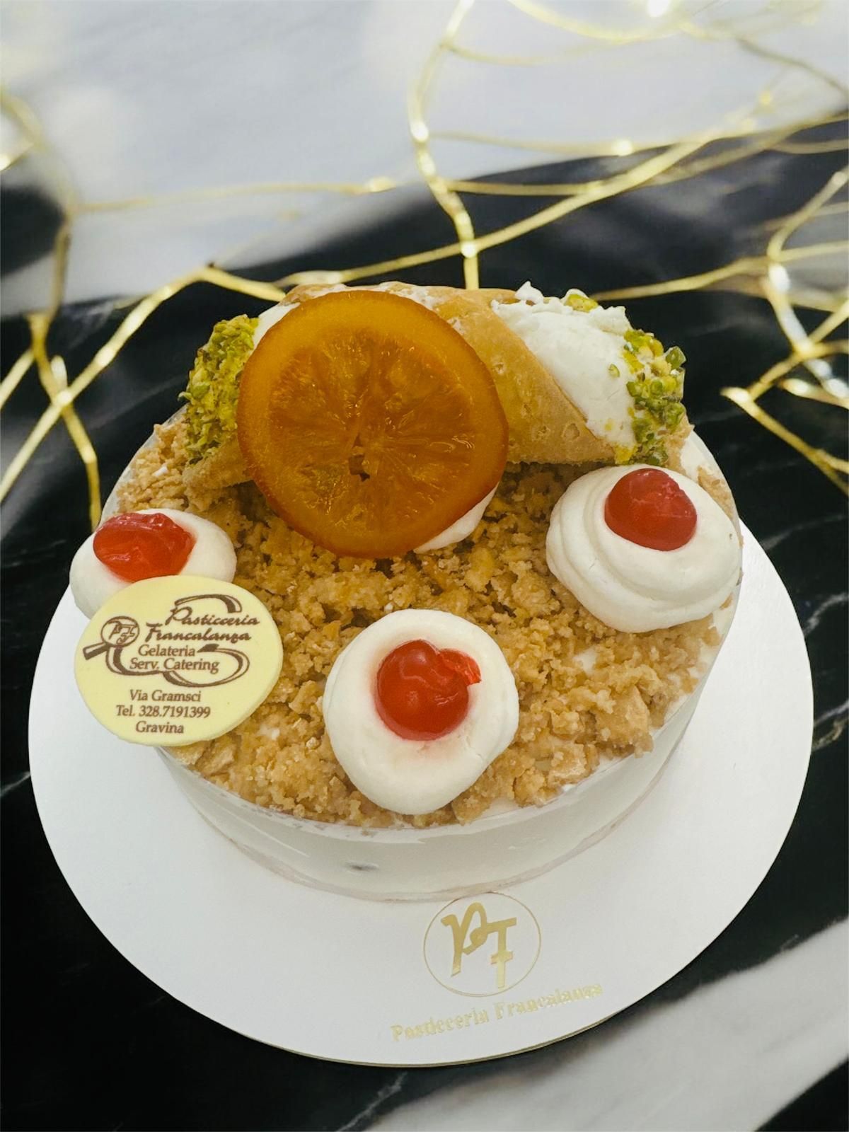 Torta rotonda con crema, biscotti sbriciolati, ciliegia, fetta d'arancia e cannoli.