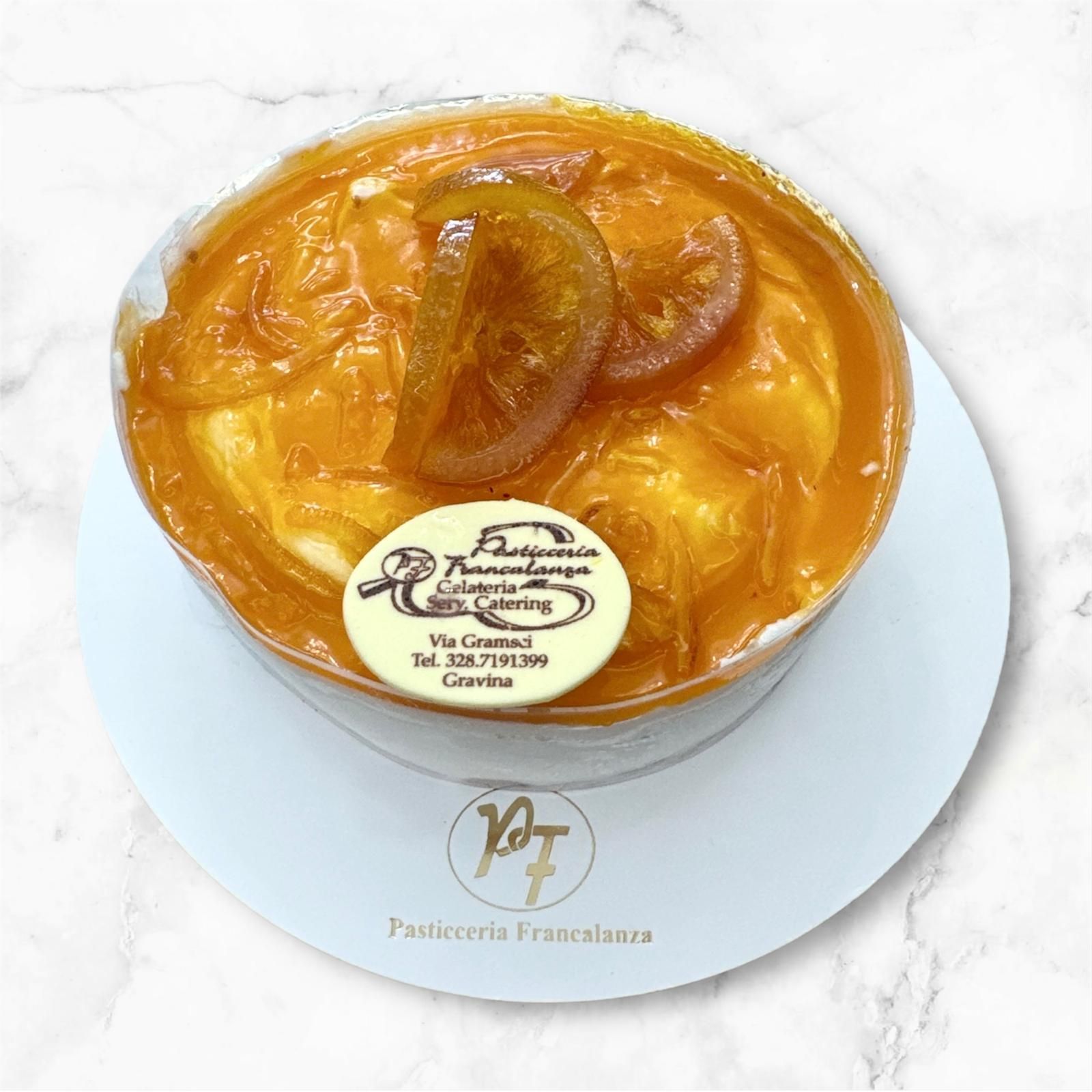 Torta all'arancia con fette di agrumi canditi su piatto bianco, logo del marchio.