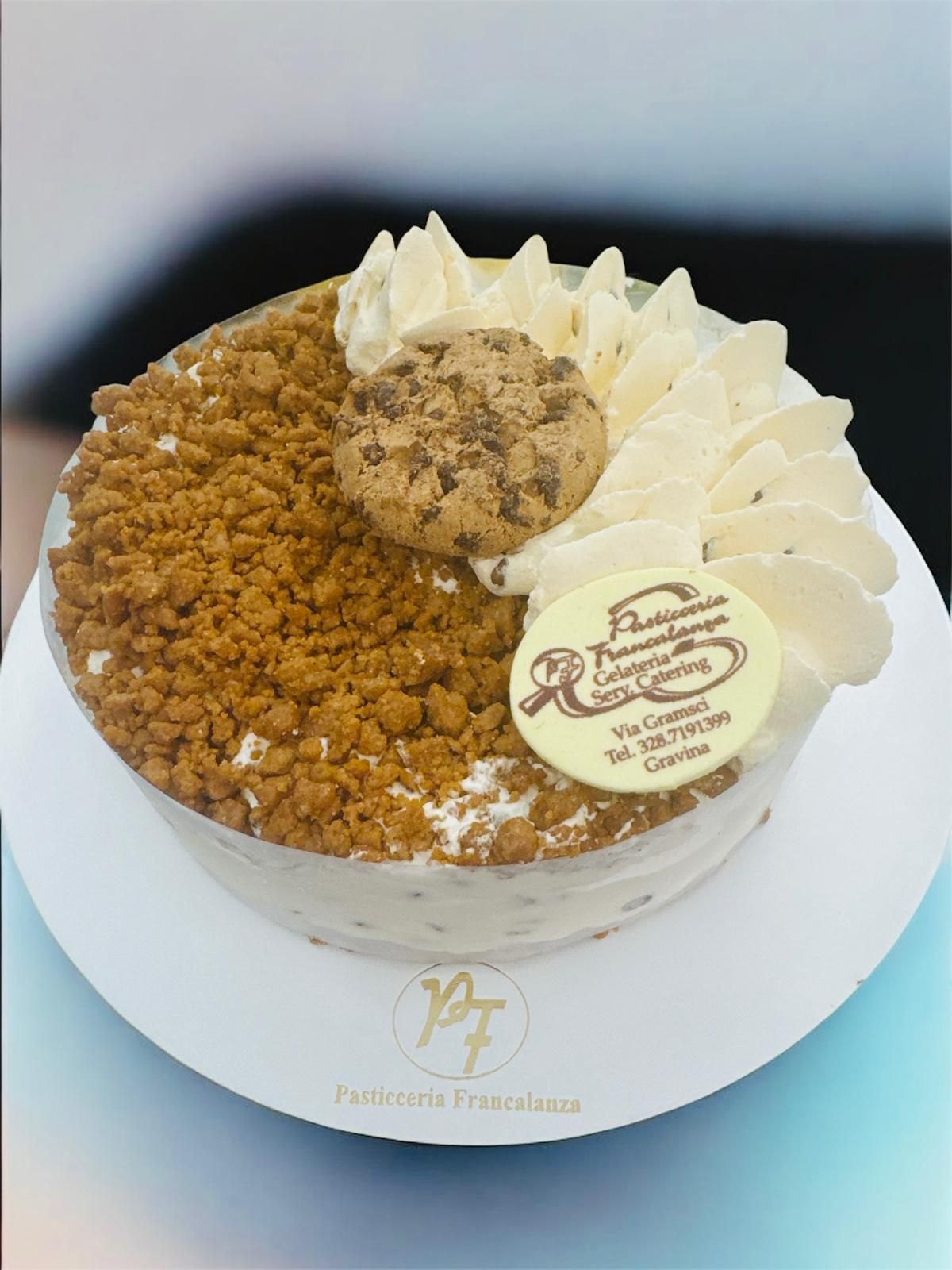 Torta con biscotti, vortici di crema e briciole, su un piatto bianco.