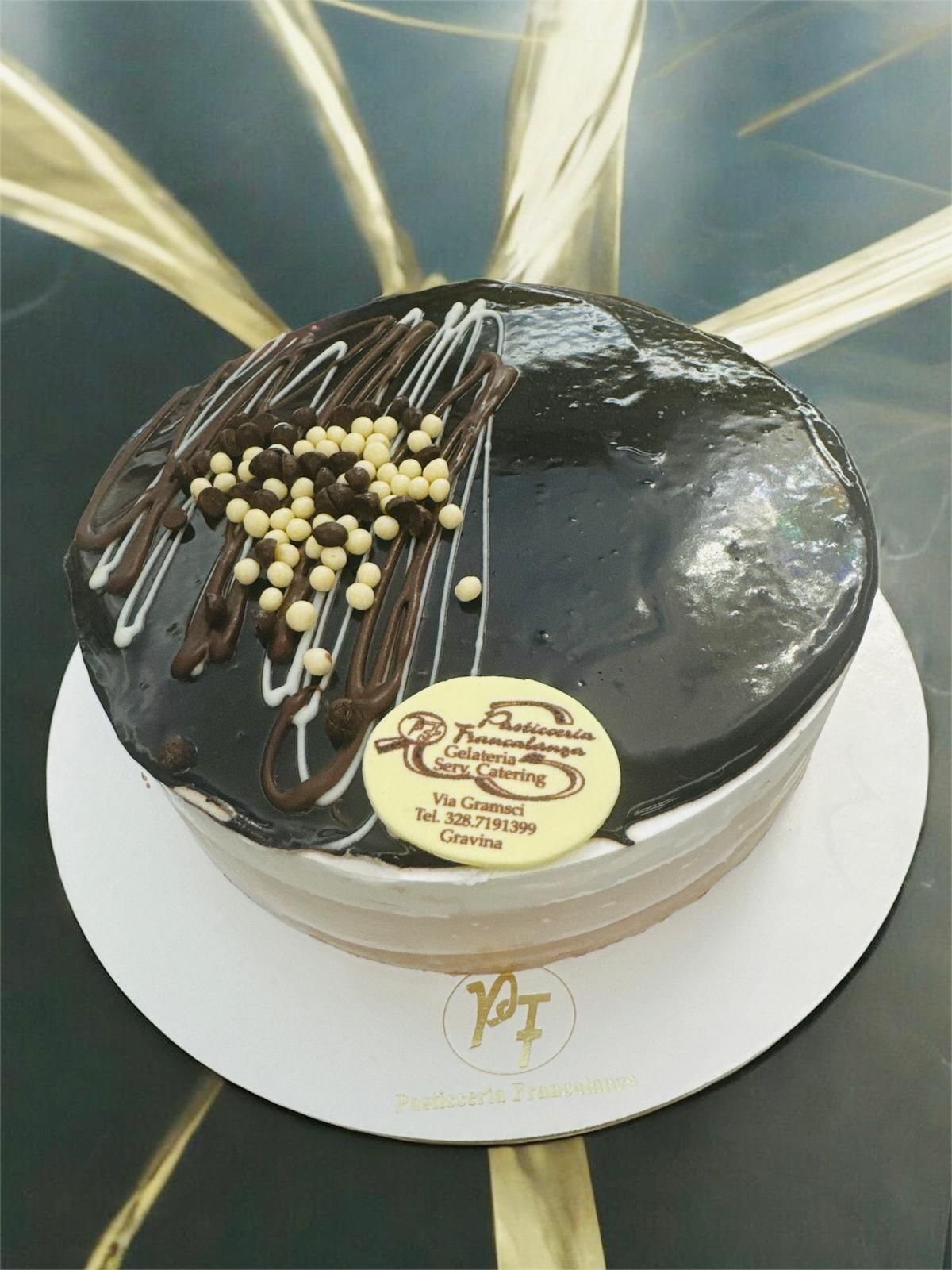 Torta al cioccolato con glassa fondente e gocce di cioccolato bianco, decorata con palline di cioccolato bianco, su un piatto bianco.