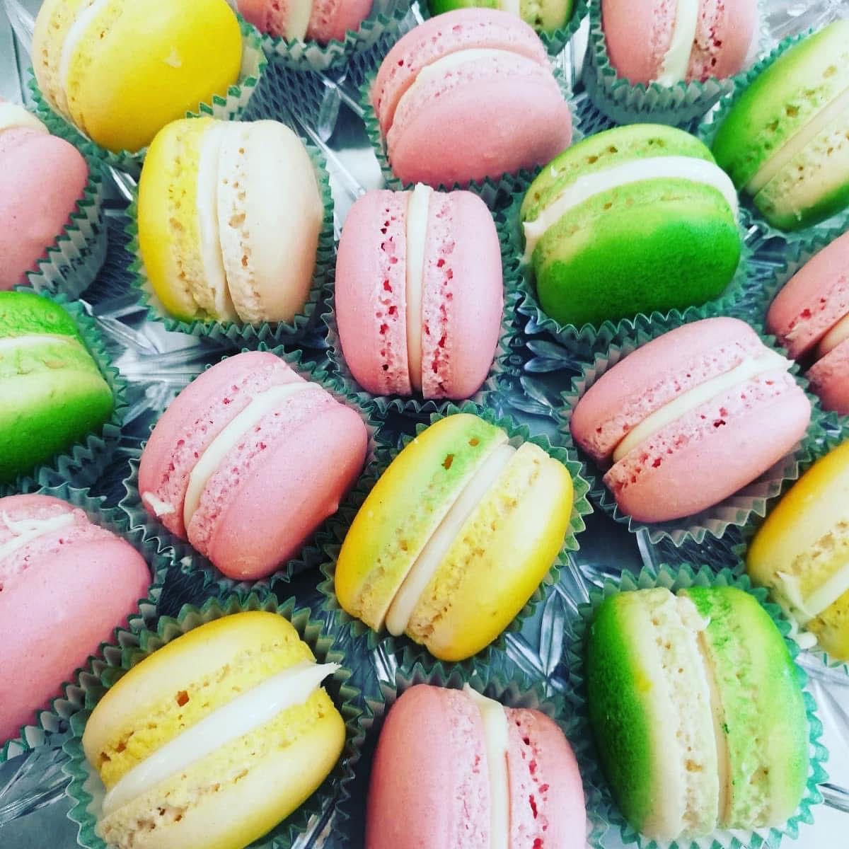Macaron colorati, rosa, gialli e verdi, disposti su un vassoio di vetro.