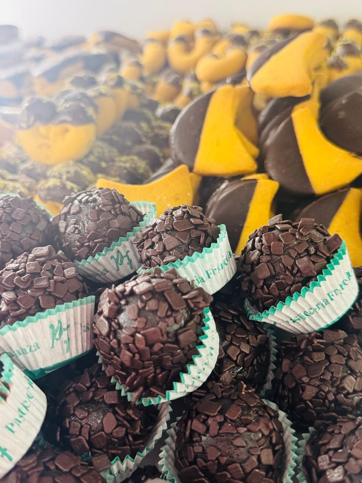 Tartufi al cioccolato in bicchieri di carta, biscotti gialli e al cioccolato in una vetrina di dolci.