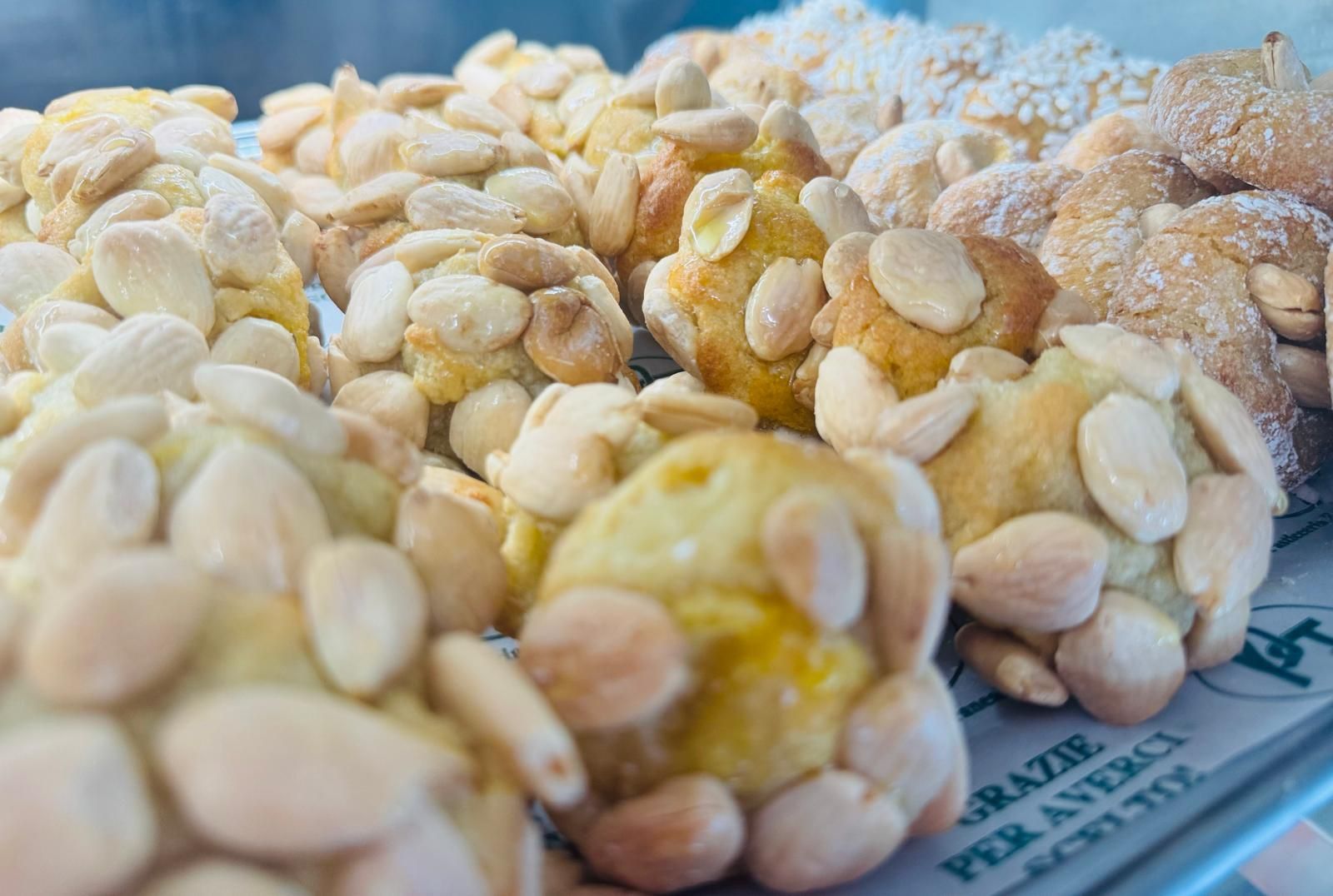 Primo piano di biscotti alle mandorle assortiti su un vassoio. Biscotti rotondi ricoperti di mandorle, alcuni con zucchero a velo.