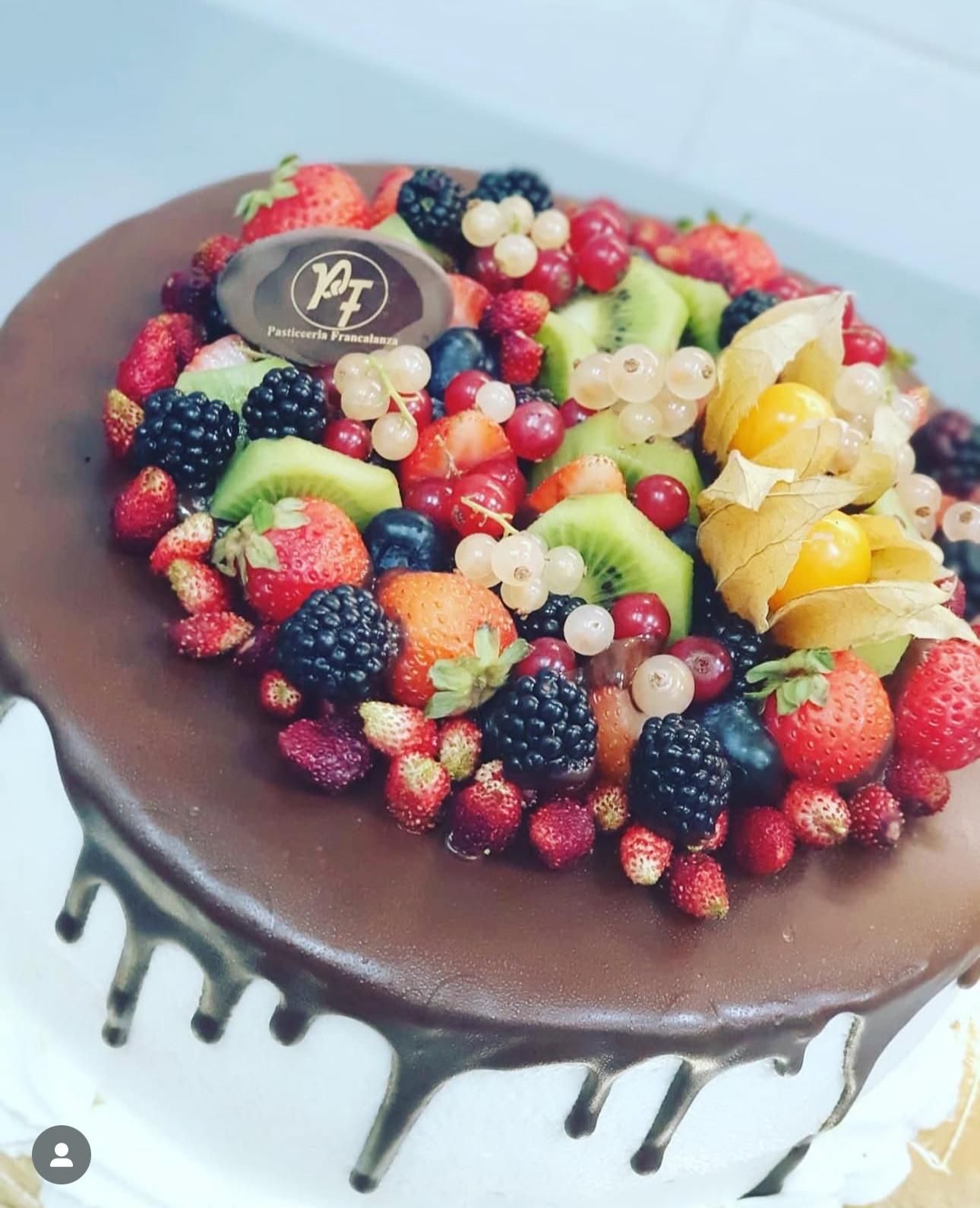 Torta al cioccolato guarnita con frutti di bosco freschi, kiwi e gocce di cioccolato.