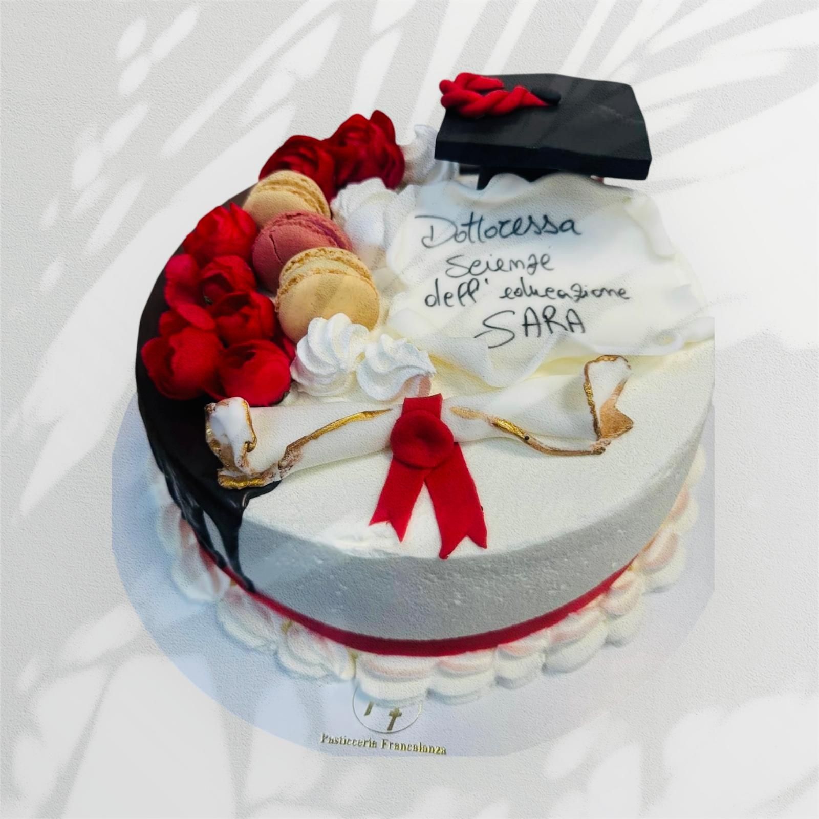 Torta di laurea con pergamena, cappello, macaron e fiori rossi. La scritta recita