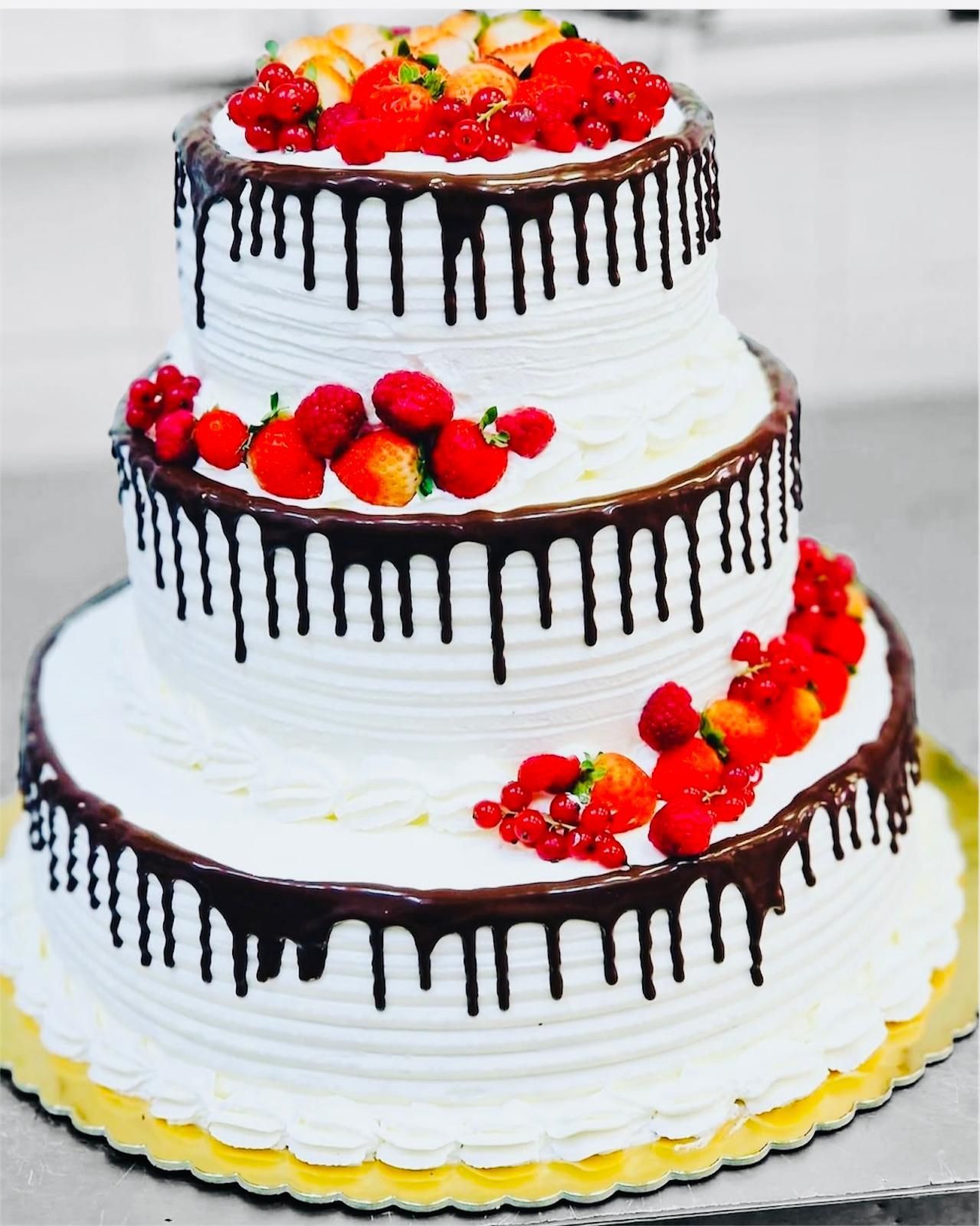 Torta bianca a tre piani con gocce di cioccolato, guarnita con bacche rosse e su una base di torta dorata.