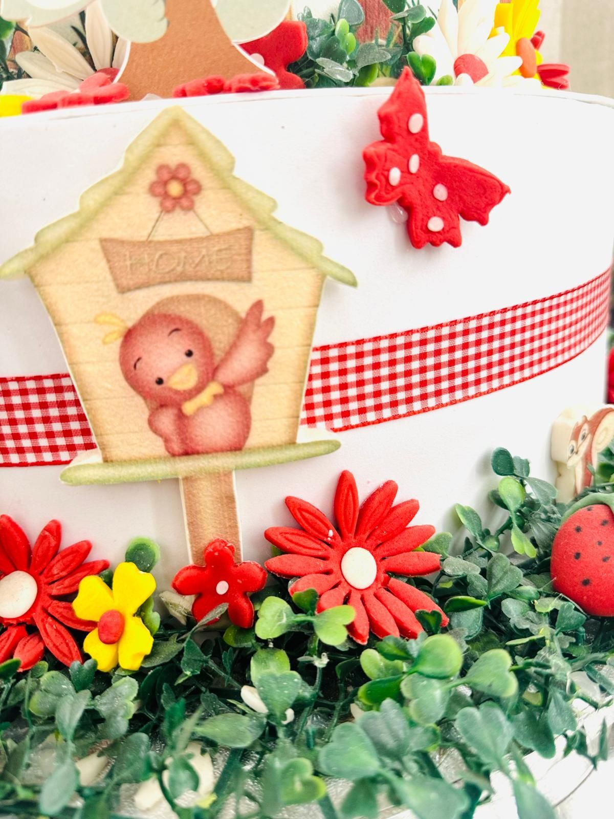 Casetta per uccelli su una torta decorata con fiori, nastro rosso a quadretti e una farfalla.